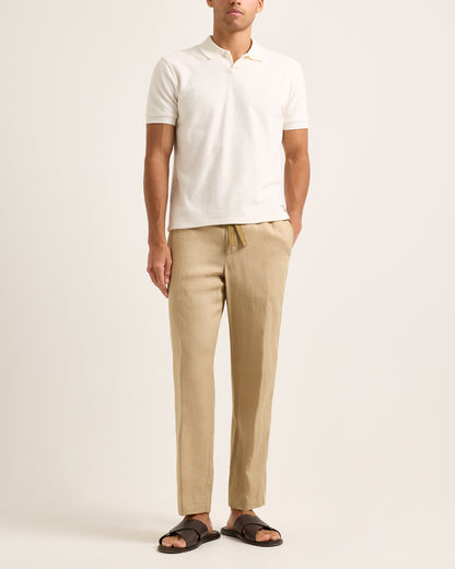 Man wearing a white polo shirt and beige pants on a plain background