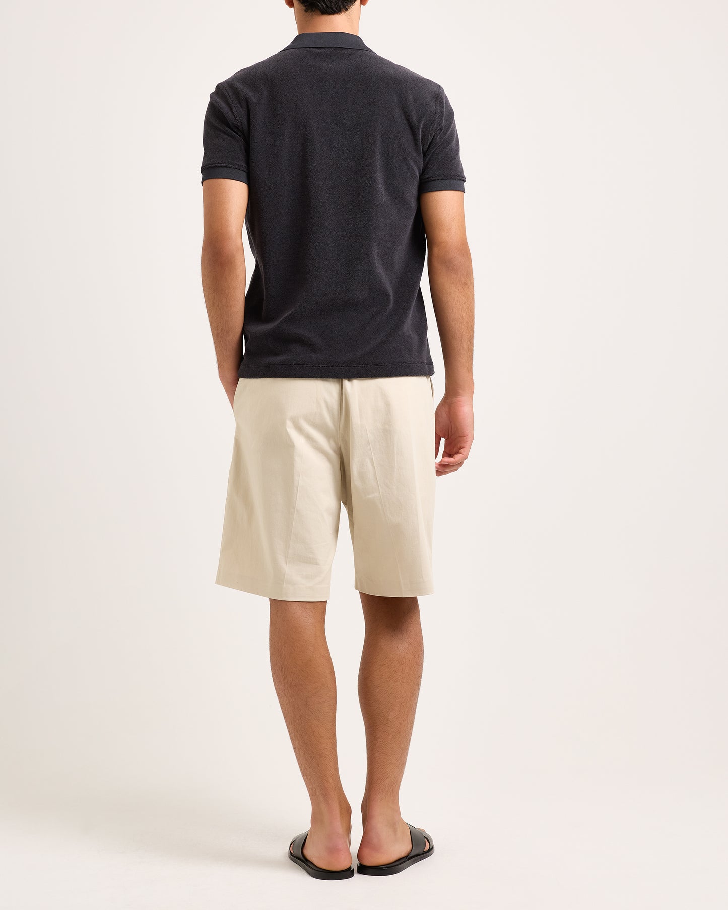 Man wearing a dark gray polo shirt with beige shorts against a light background
