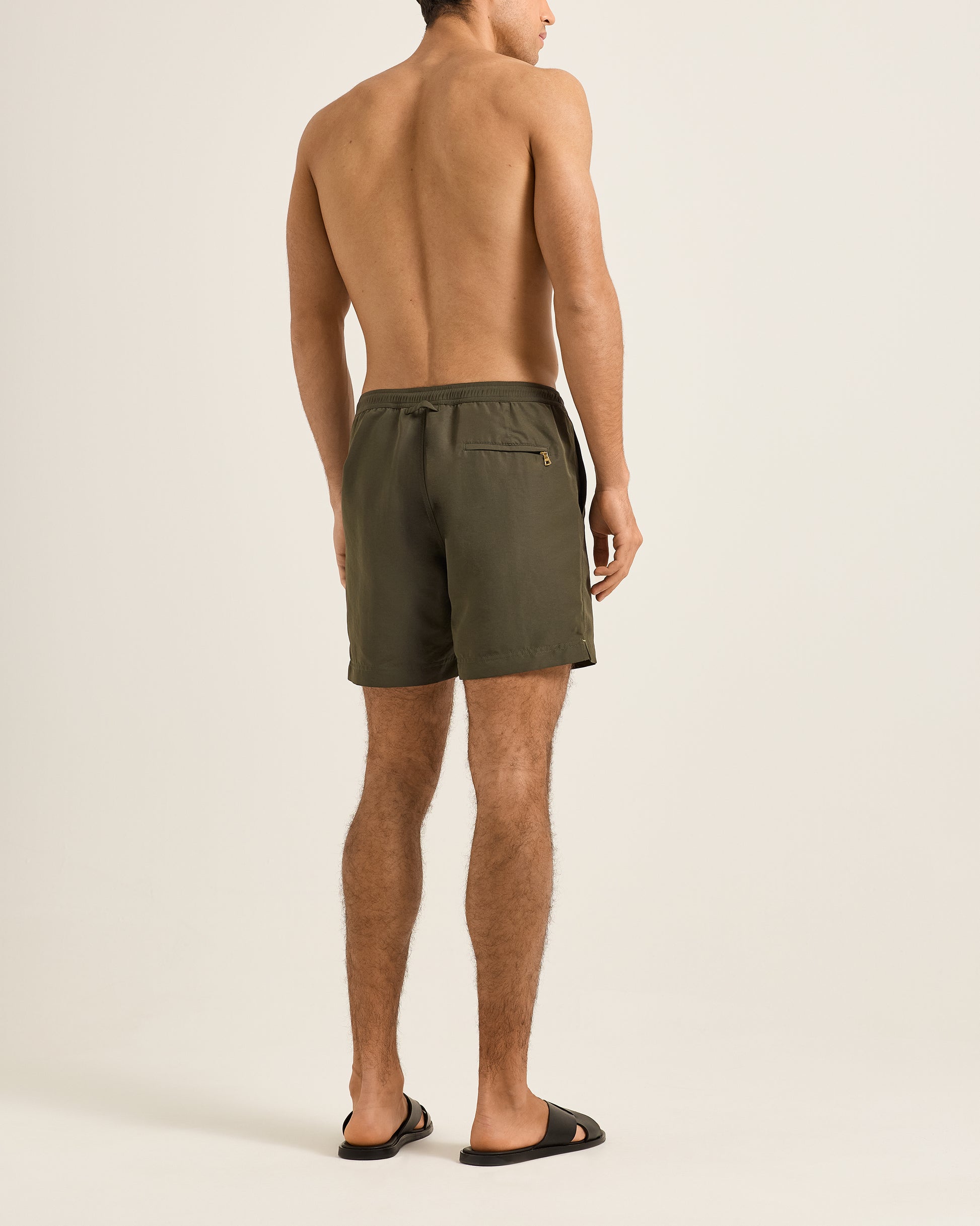Man wearing olive green swim shorts on a beige background