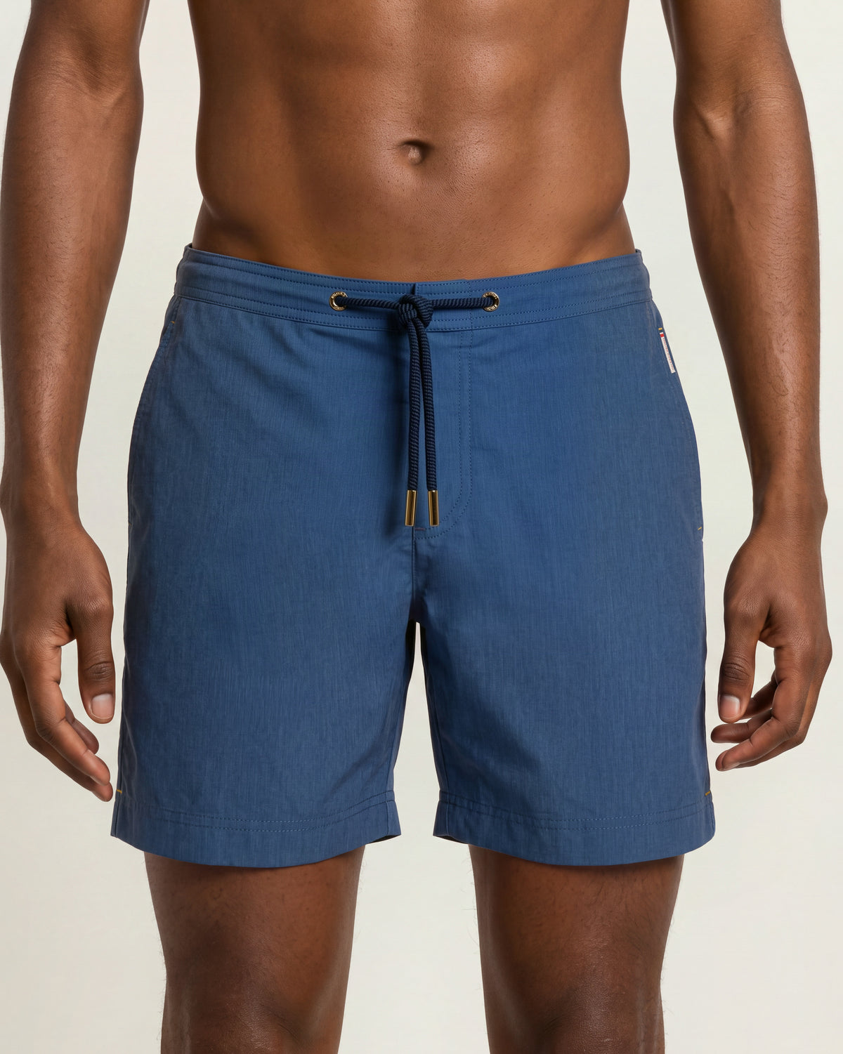 Close-up of a man wearing denim blue drawcord swim shorts with a navy robe on a plain background