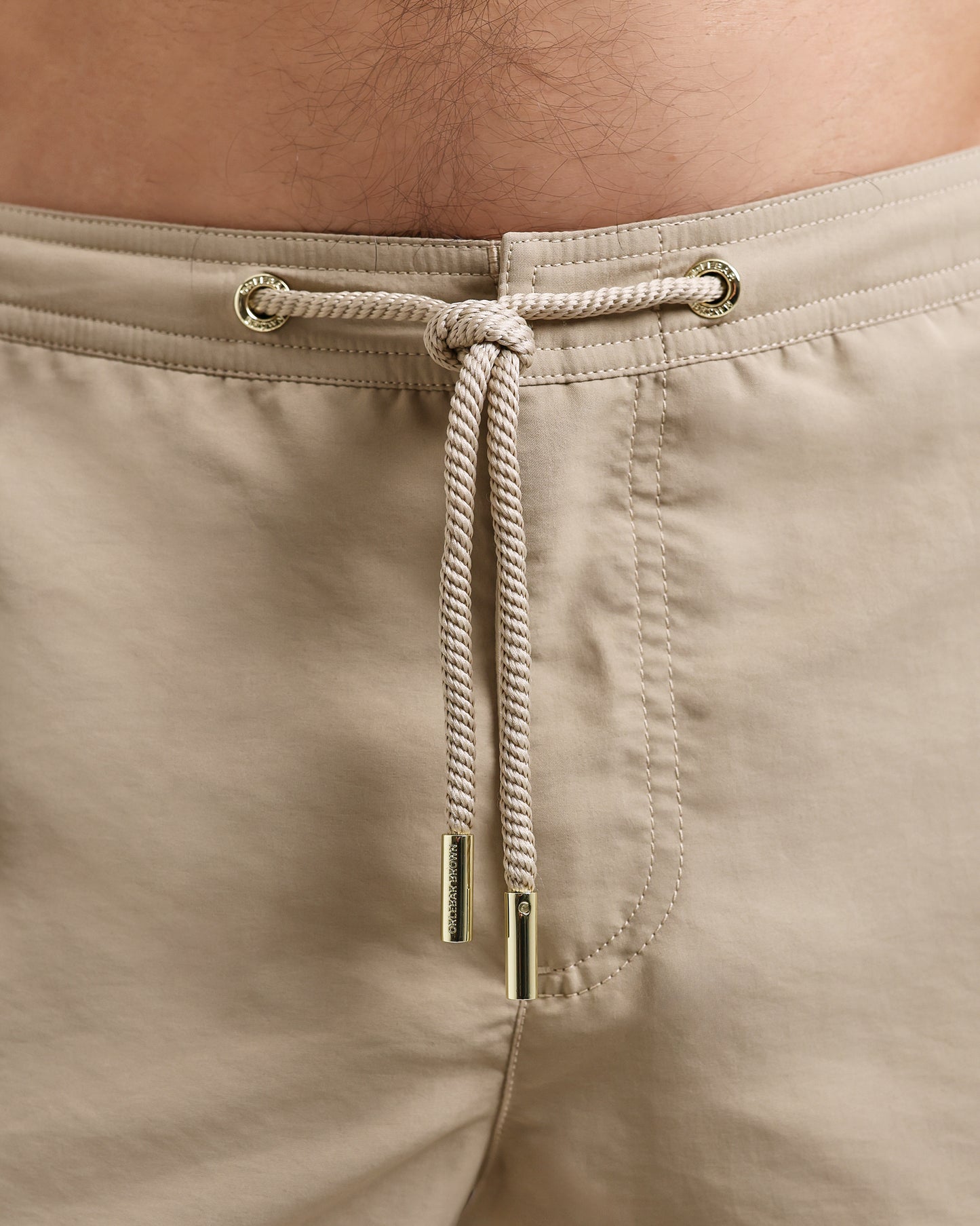 Beige shorts with a drawstring and metal buckle on a person's waist.