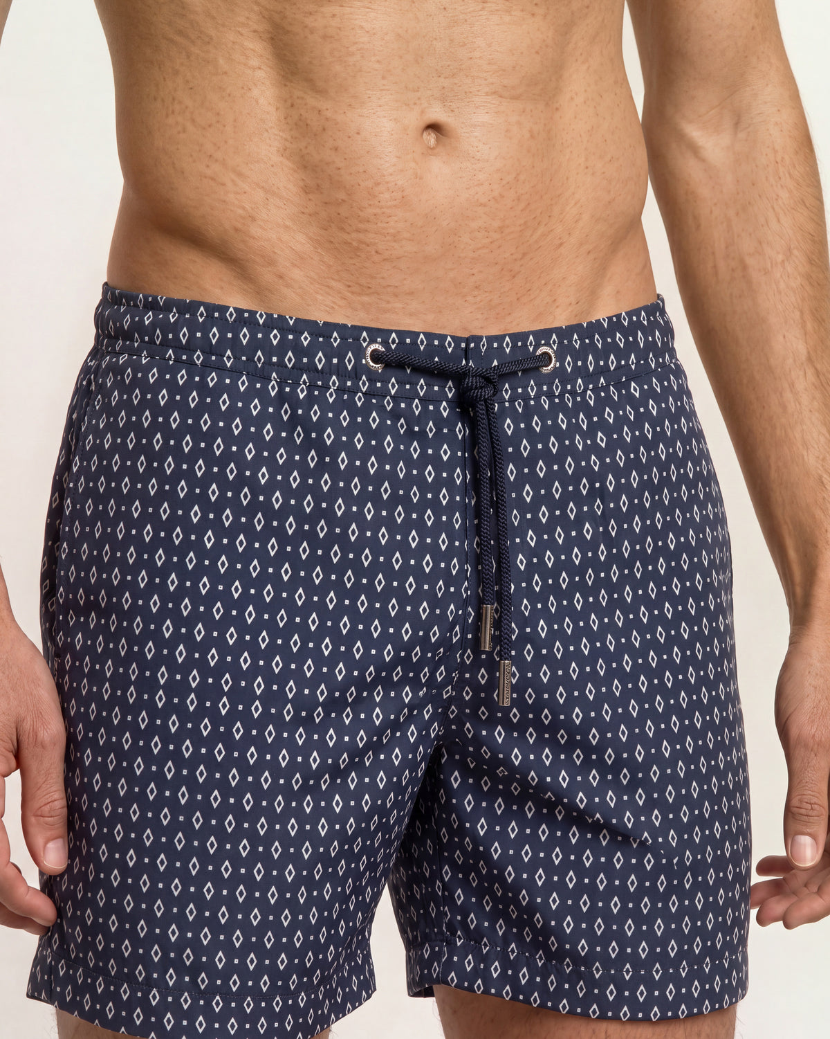 Closeup of navy drawcord swim shorts with small white diamond print on a plain background