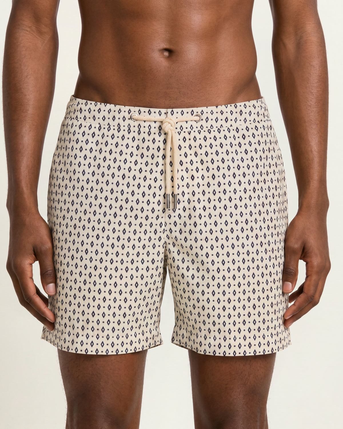 Close-up of a man wearing beige patterned drawcord swim shorts on a plane background
