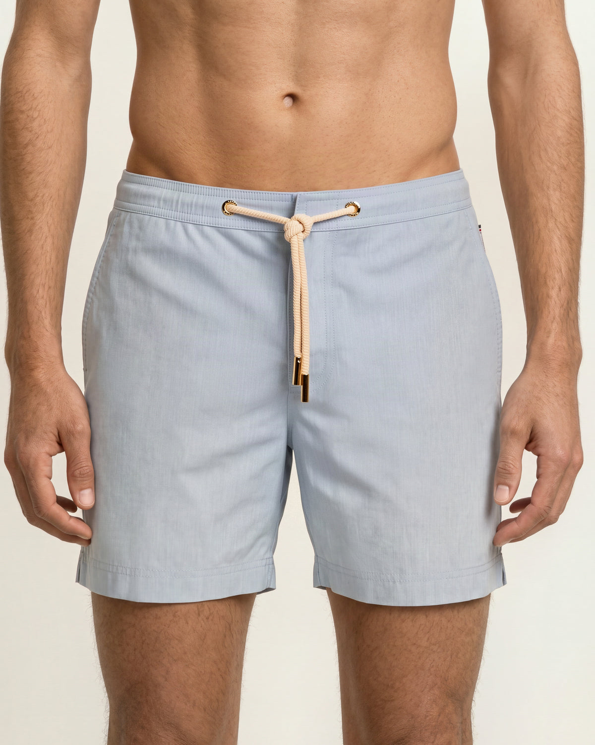 Close-up of a man wearing light blue drawcord swim shorts on a plain background