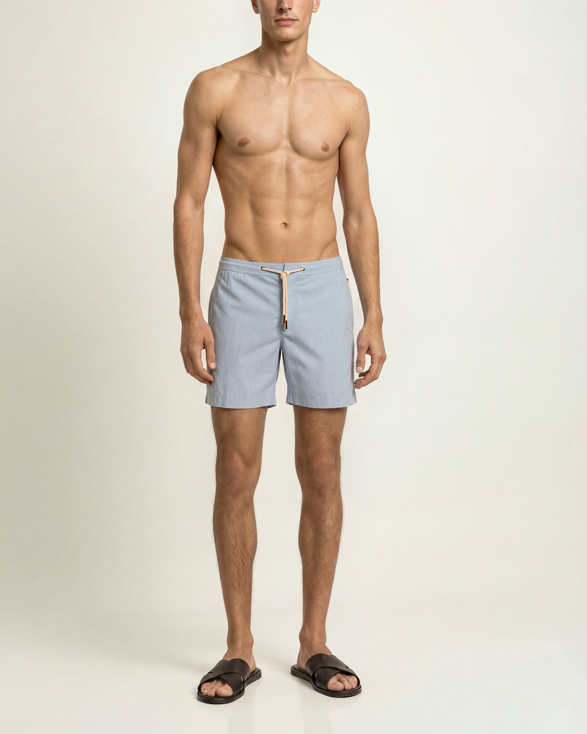 Man wearing light blue drawcord swim sorts and brown sandals on  a plain background