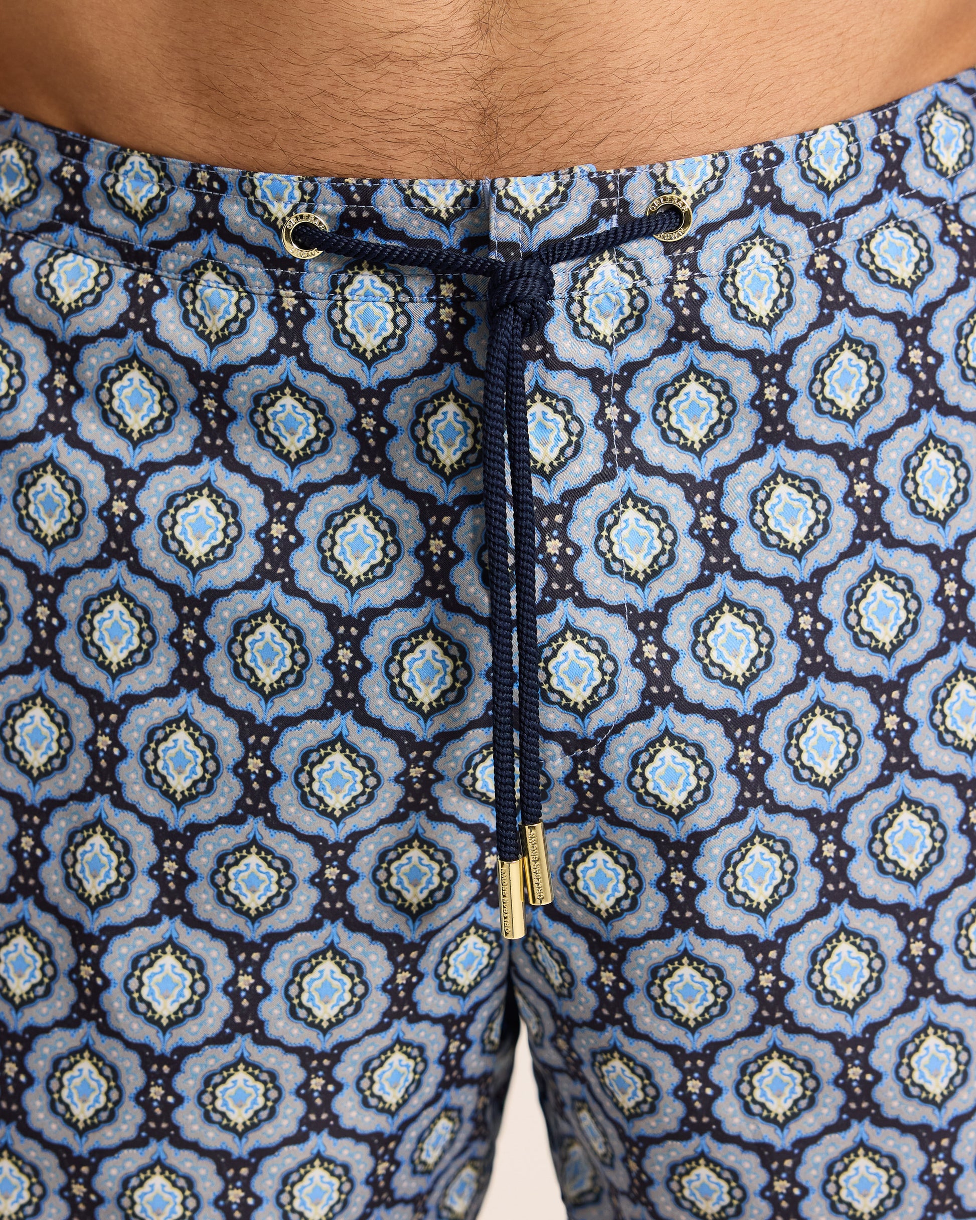 Close-up of patterned shorts with a drawstring and gold button.