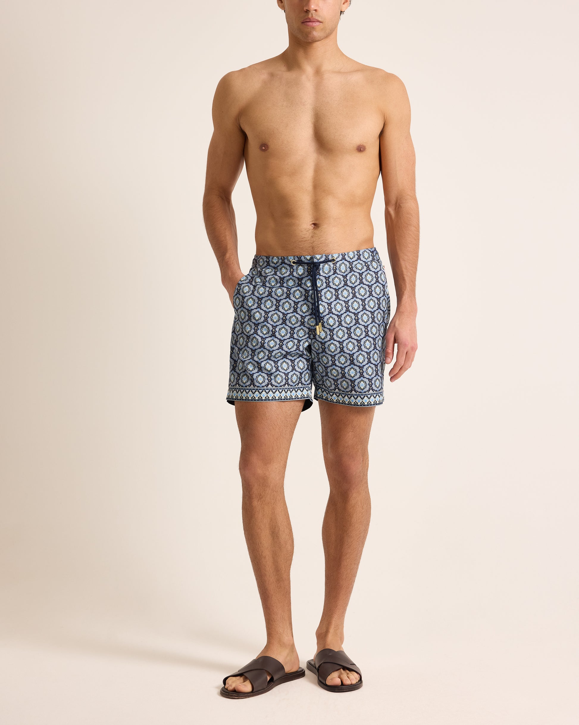 Man wearing navy geometric print swim shorts with drawcord waist on a plain background