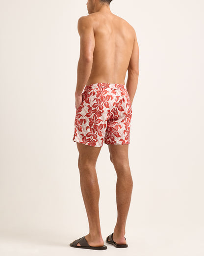 Man wearing red floral swim shorts on a white background