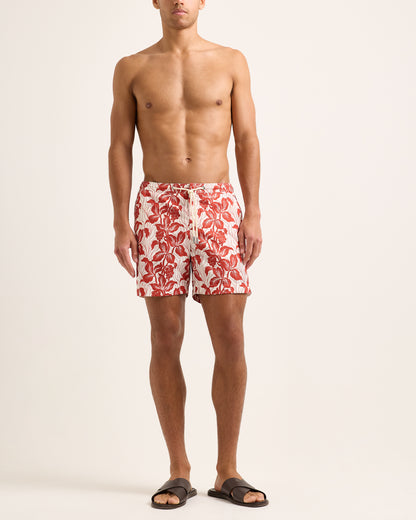 Man wearing red floral swim shorts on a white background