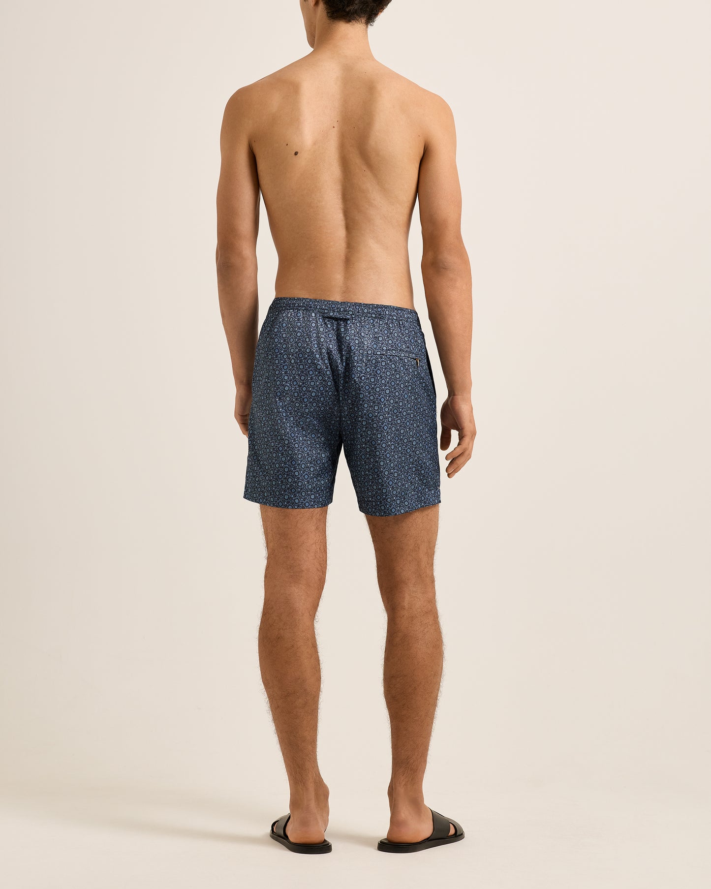 Man wearing blue patterned swim shorts on a beige background