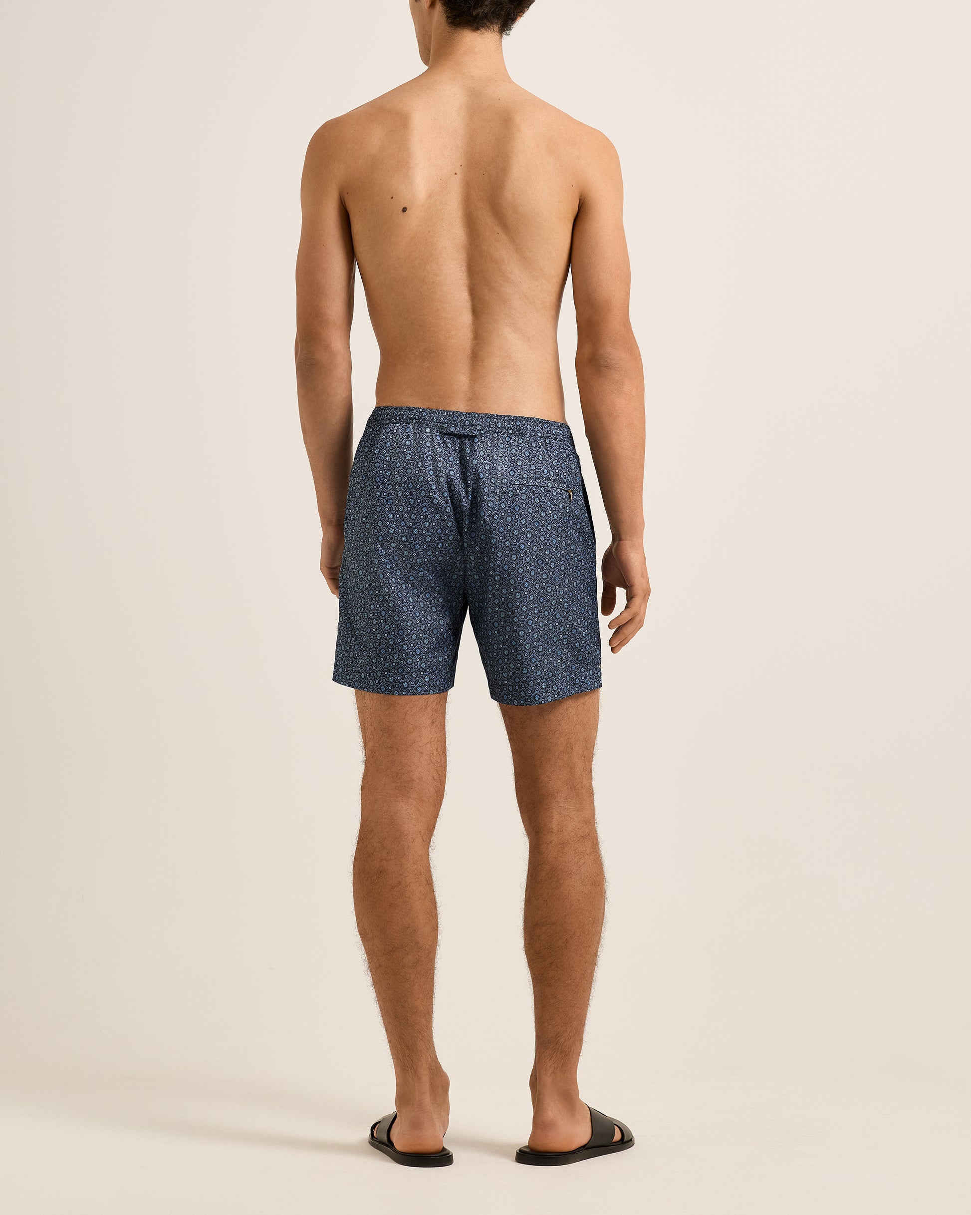 Man wearing blue patterned swim shorts on a beige background