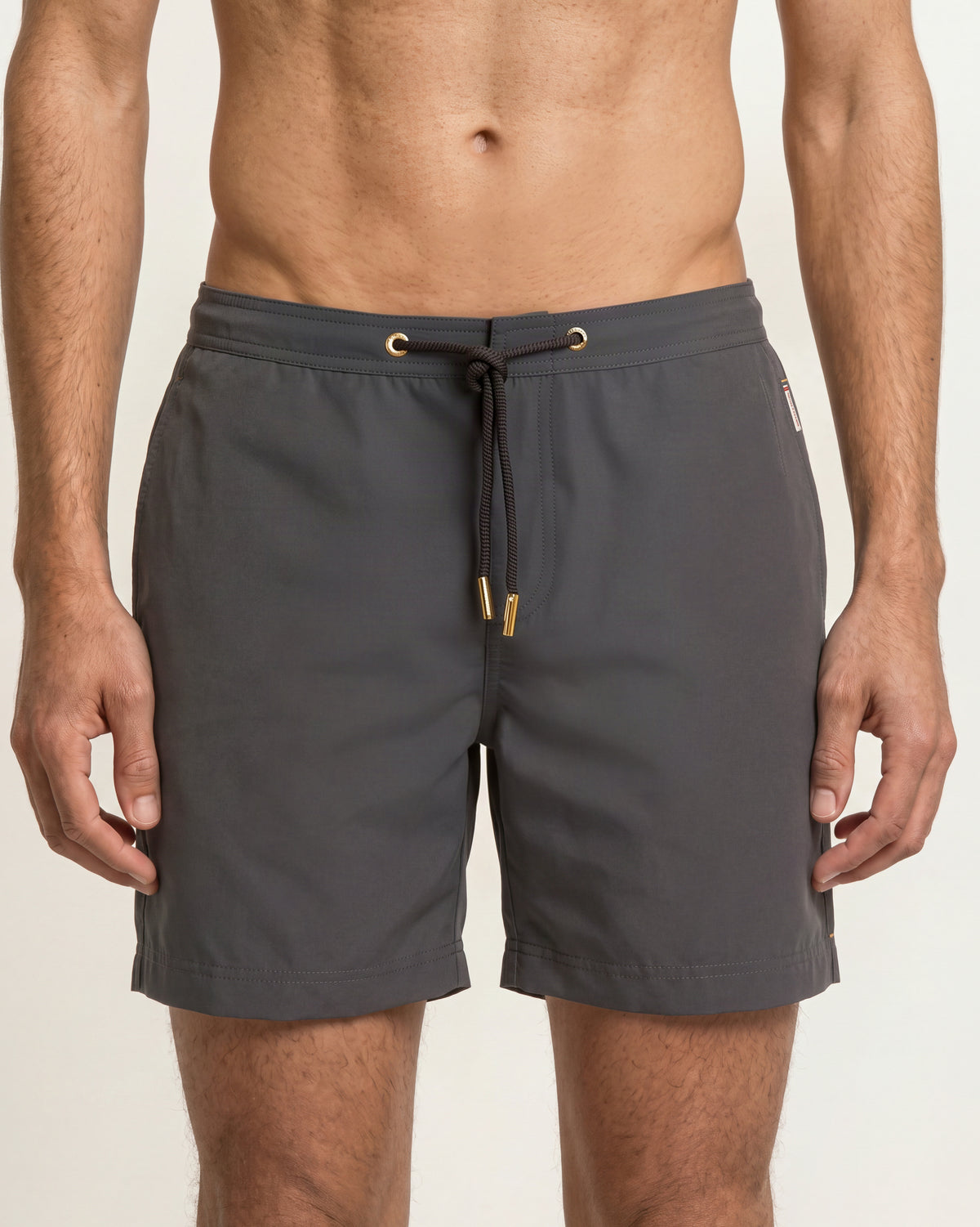 Closeup of grey drawcord swim shorts with gold cord detailing on a plain background