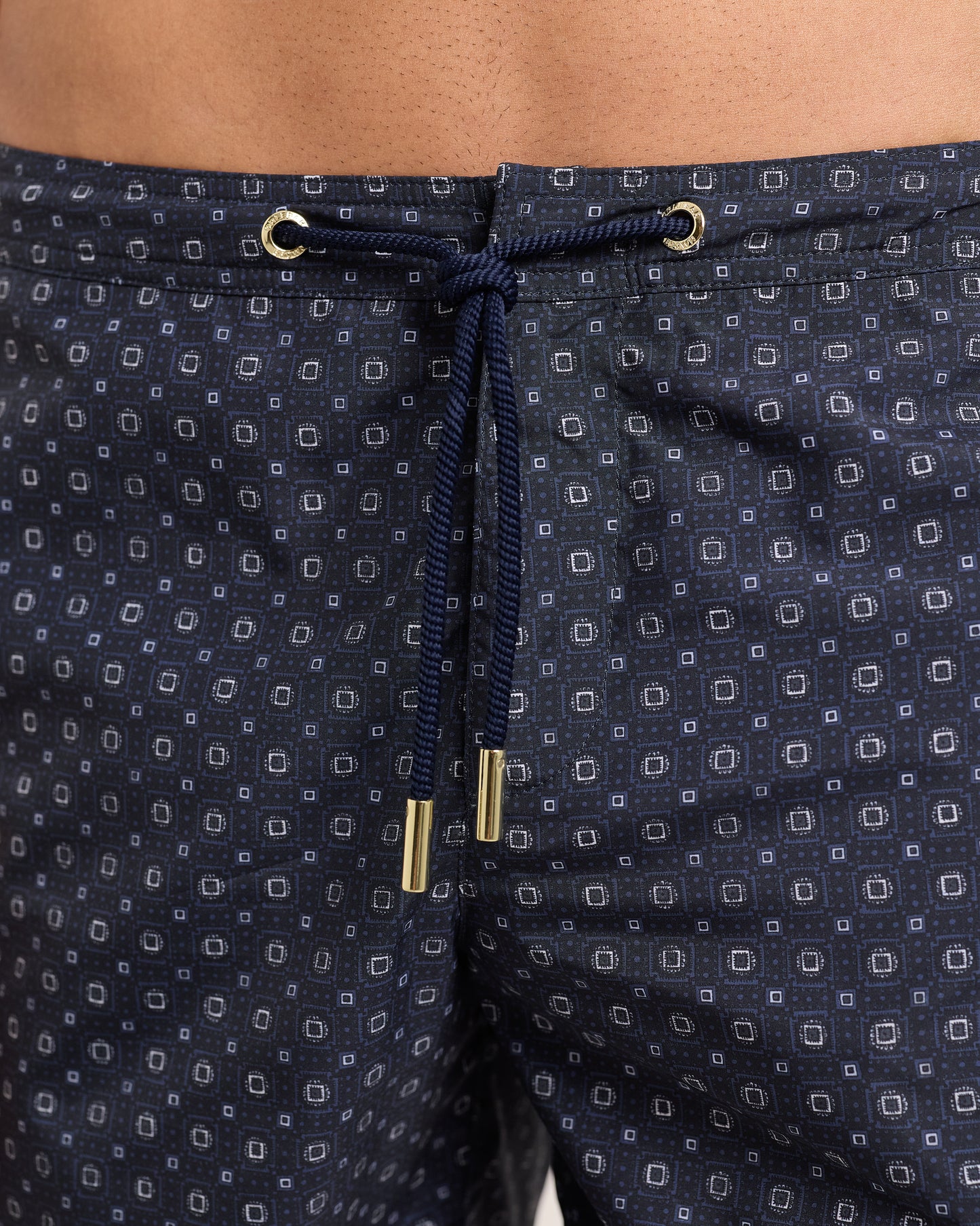 Navy patterned shorts with drawstring and gold accents on a matching background