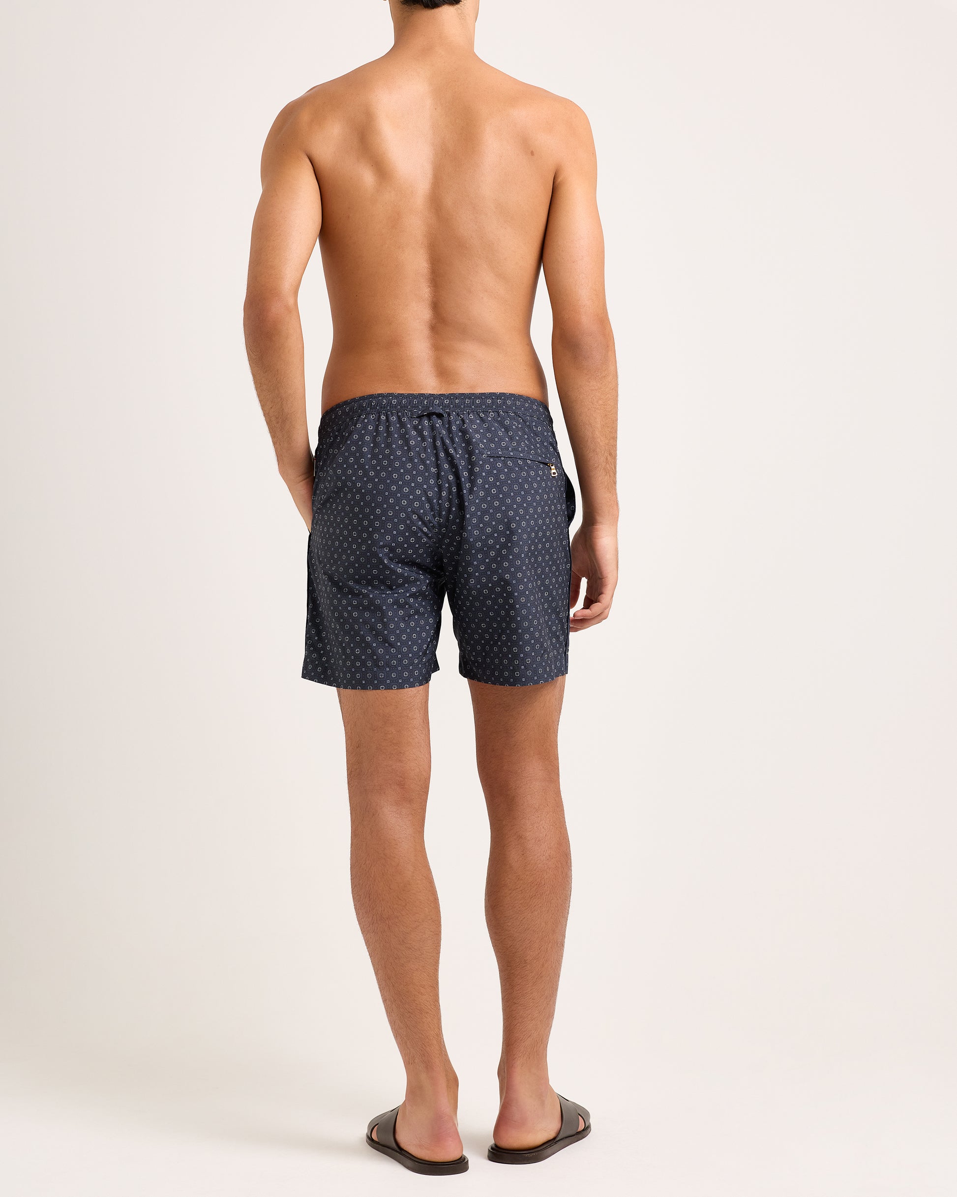 Man wearing dark blue swim shorts with geometric pattern and drawstring waist on a white background