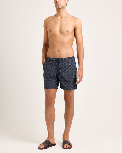 Man wearing dark blue swim shorts with geometric pattern and drawstring waist on a white background