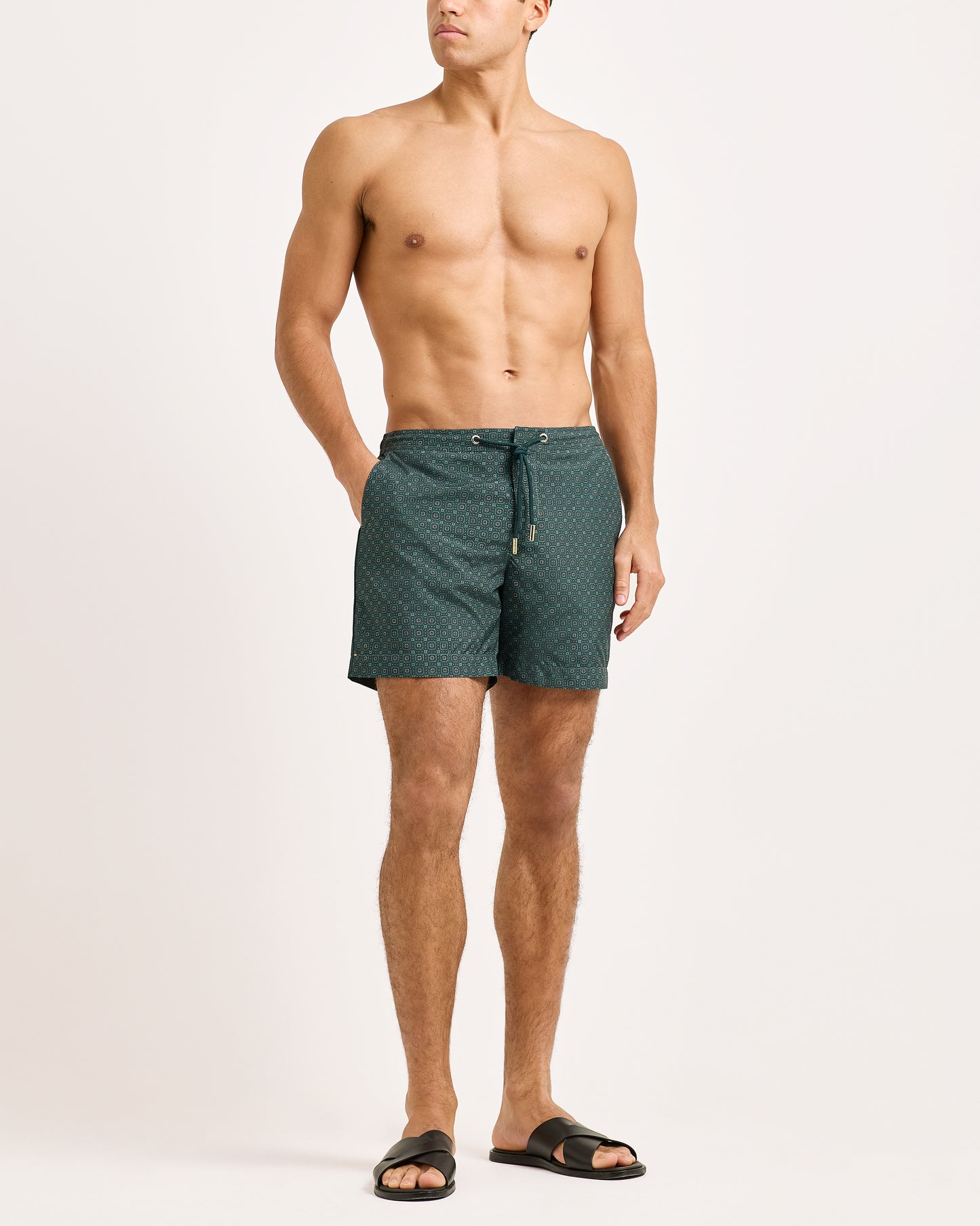 Man wearing green patterned swim shorts on a white background