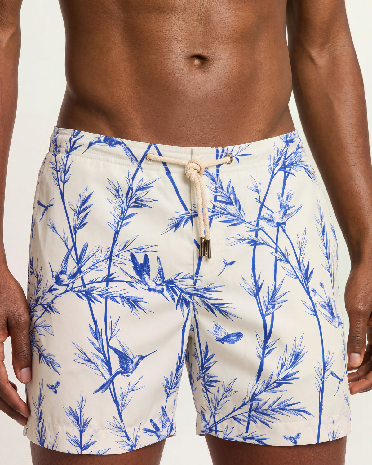Close-up of a man wearing white drawcord swim shorts with blue pattern on a plain background