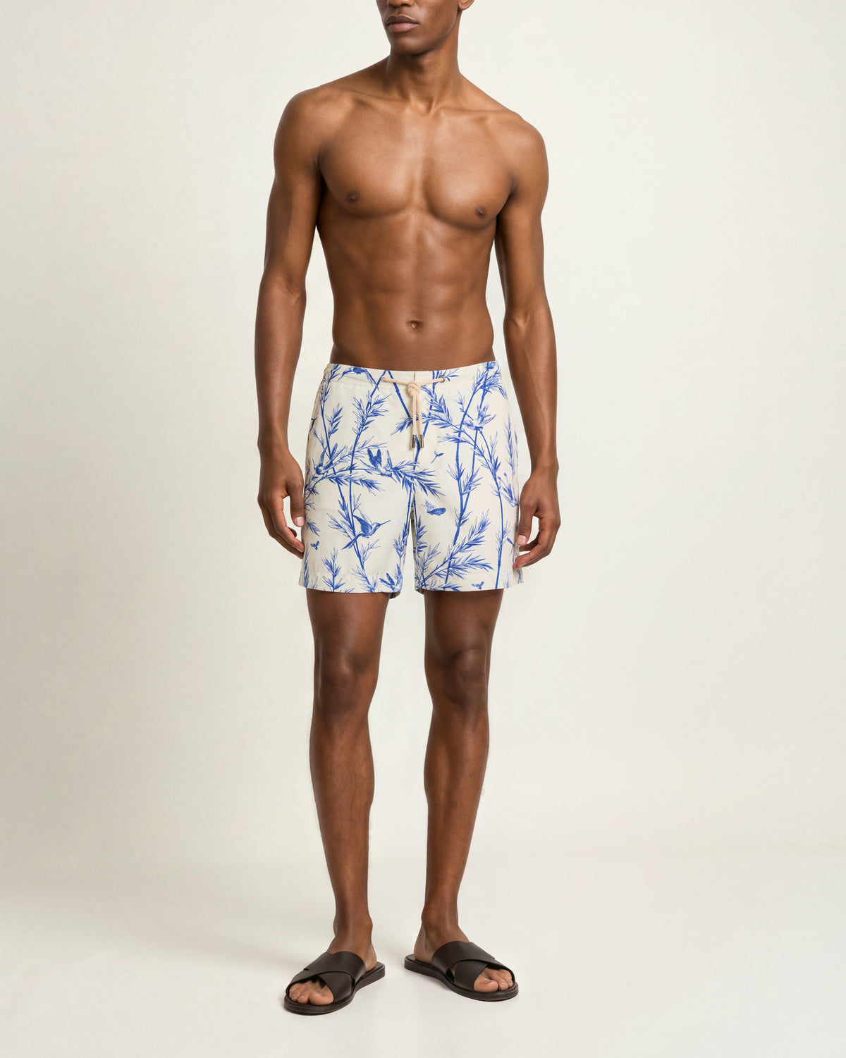 Man wearing white drawcord-waist swim shorts with a blue pattern on a plain background