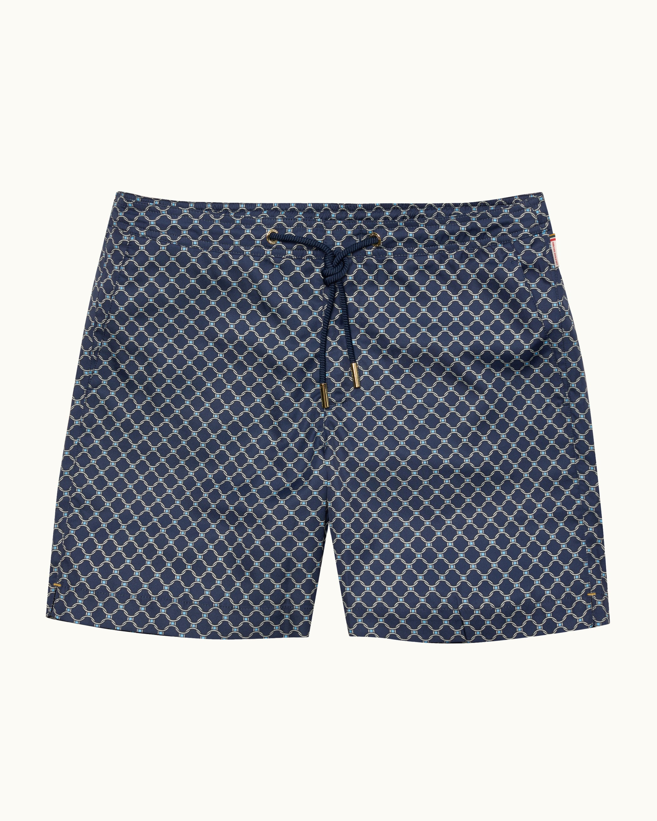 A pair of men's swim trunks featuring a navy blue and white geometric trellis pattern, with a matching navy drawstring at the elastic waistband, shown flat against a light cream background.