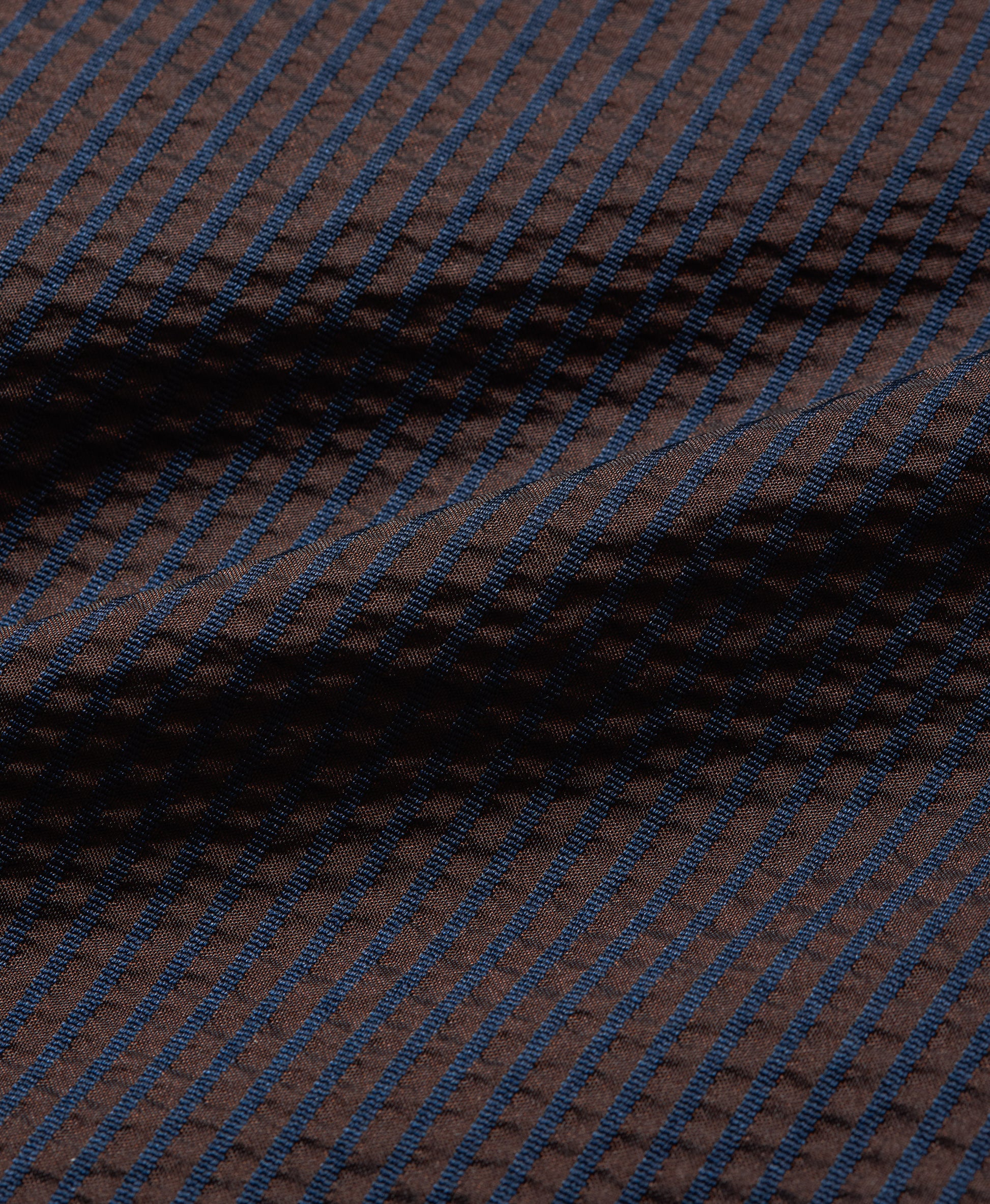 A close-up of a textured fabric with a dark brown base and thin, repeating blue diagonal stripes.