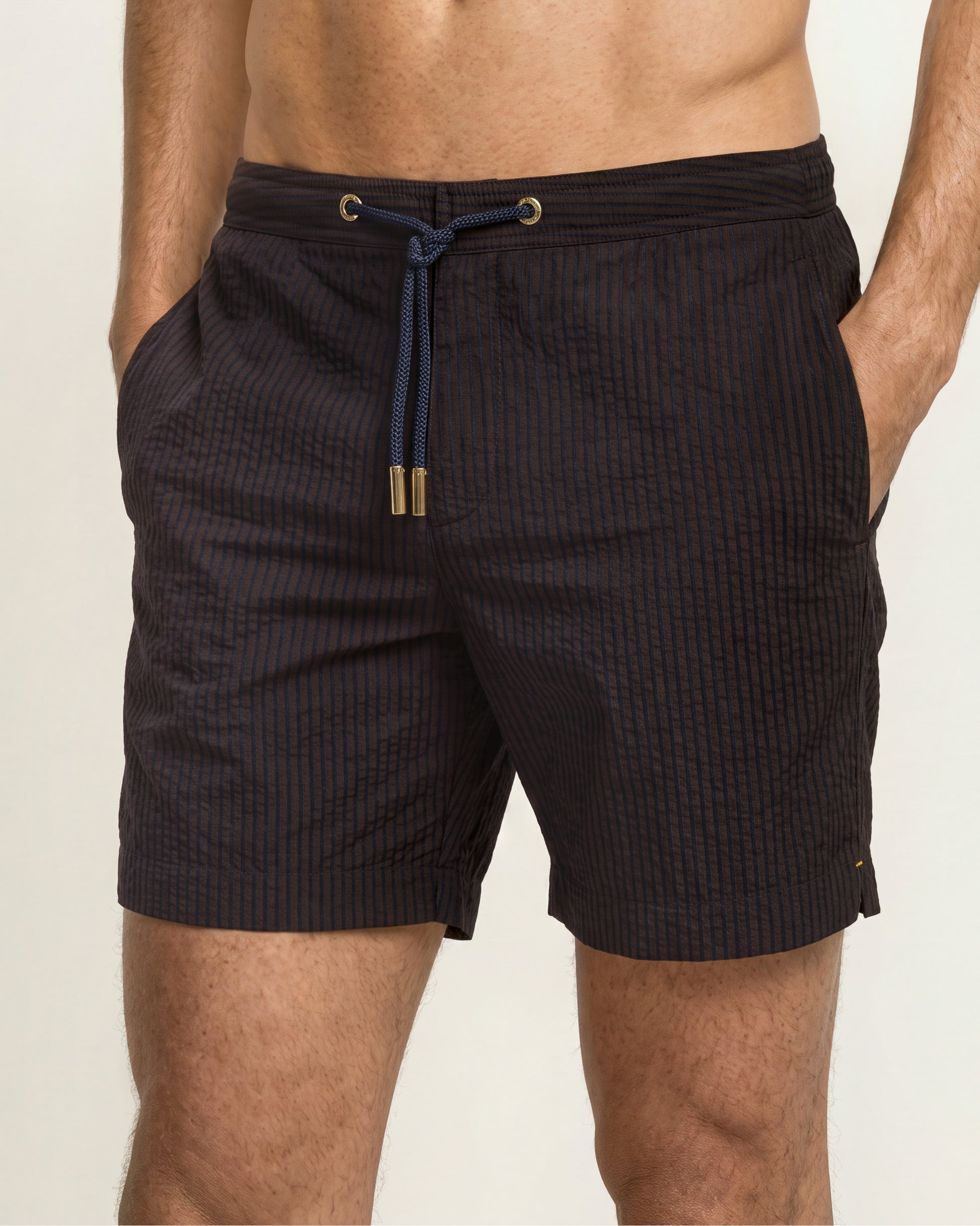 A close-up of a man wearing dark charcoal textured swim trunks with a navy blue drawstring and gold-tone hardware.