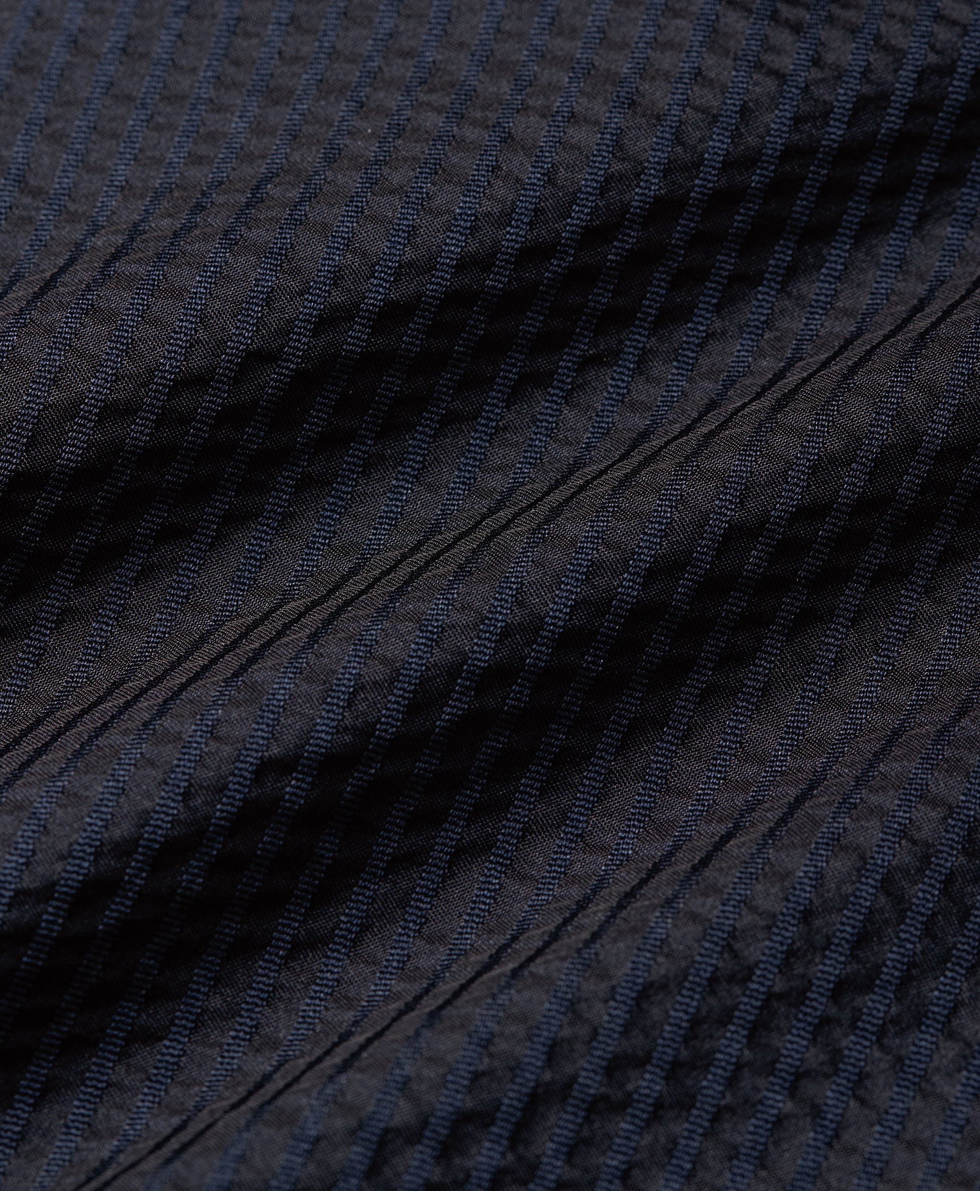 Close-up of a dark navy blue textured fabric with fine vertical ribbing and diagonal stitched details.