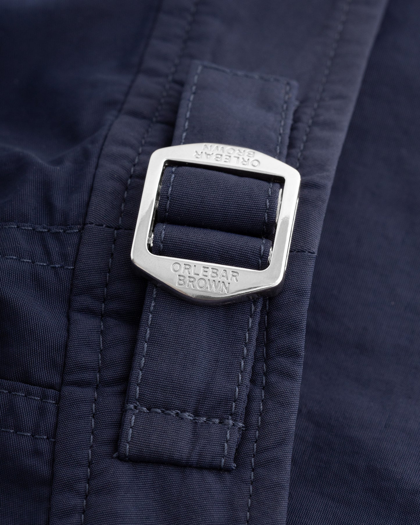 Close-up of a dark navy blue garment with a silver metal buckle closure. The buckle is engraved with the brand name