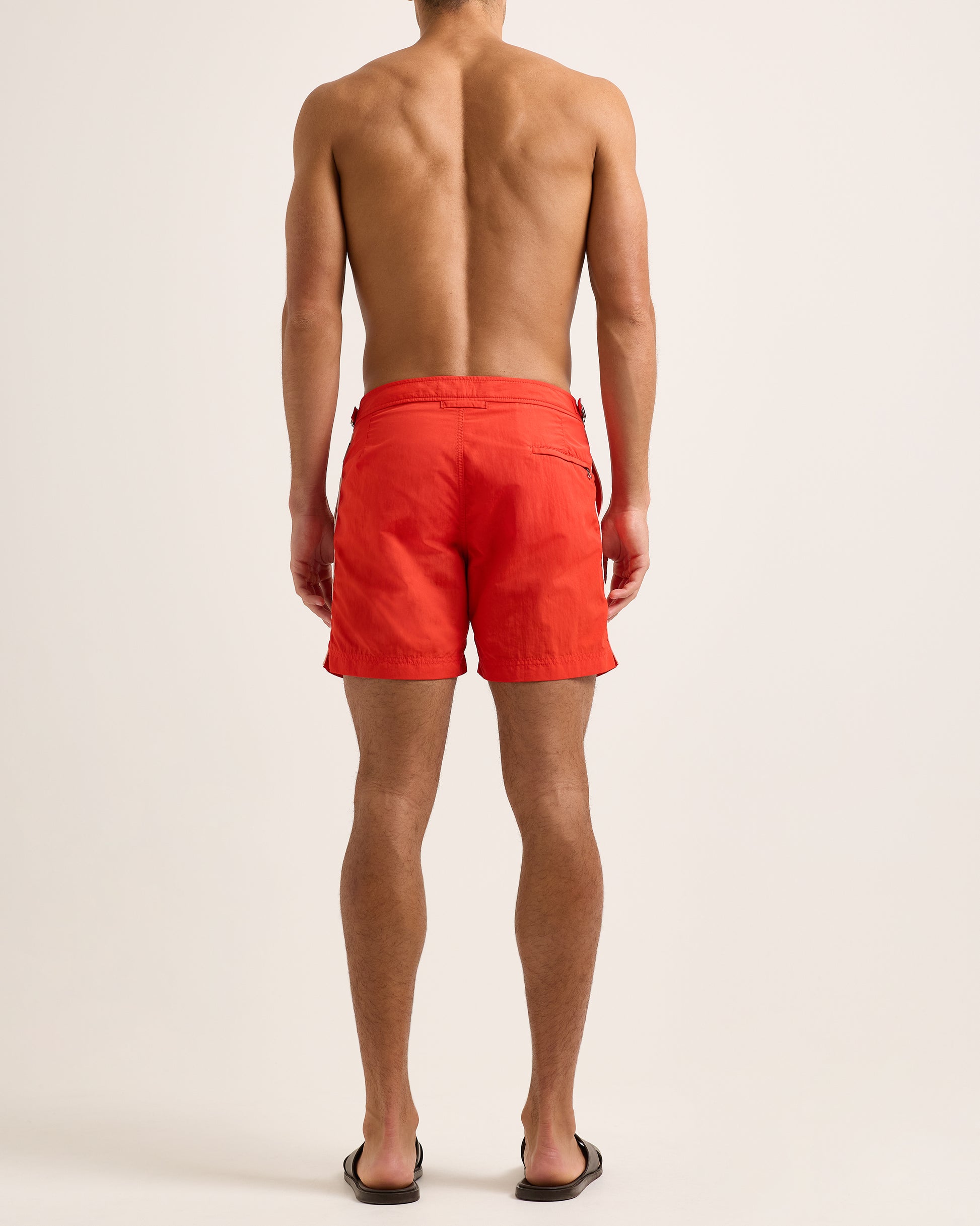 Man wearing red swim shorts with white side stripe on light background