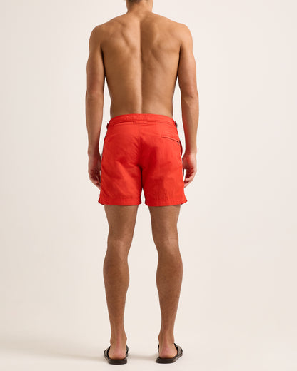 Man wearing red swim shorts with white side stripe on light background