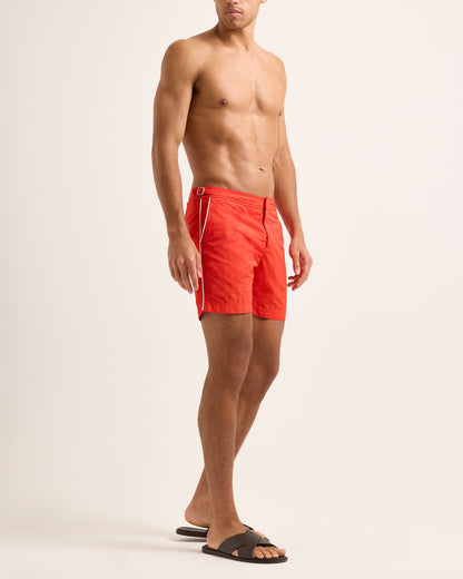 Man wearing red swim shorts with white side stripe on light background