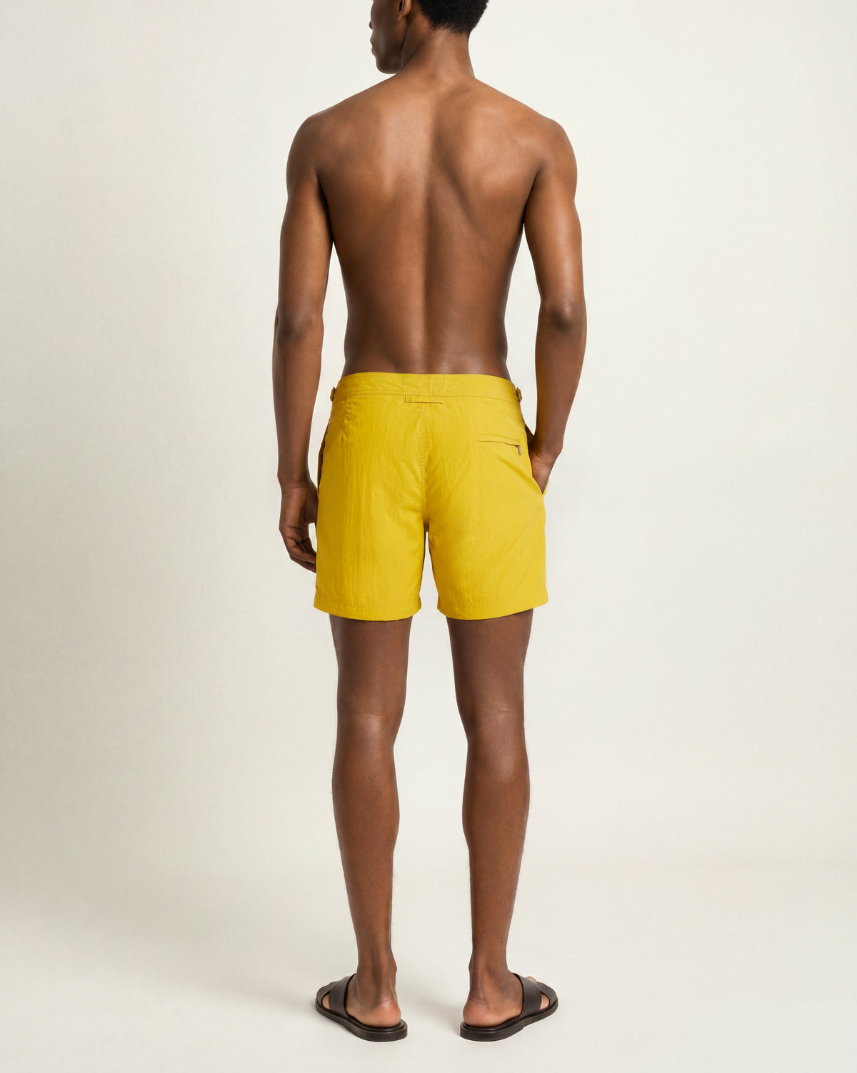 Man wearing yellow swim shorts and brown sandals on a plain background