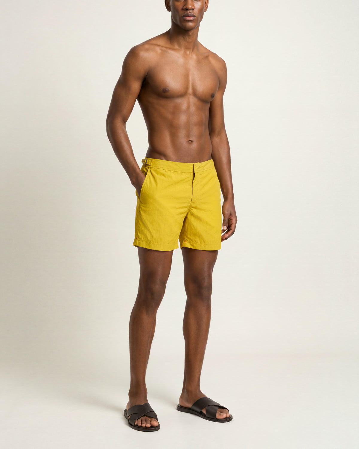 Man wearing yellow swim shorts and brown sandals on a plain background
