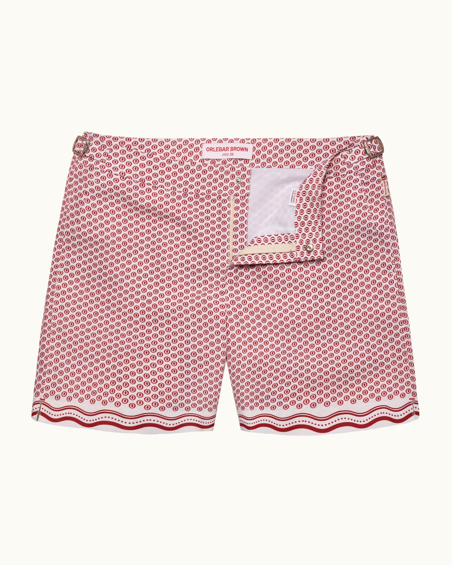 A pair of swimshorts featuring a pink and white geometric pattern with a scalloped wavy hem and a white brand label at the waistband.