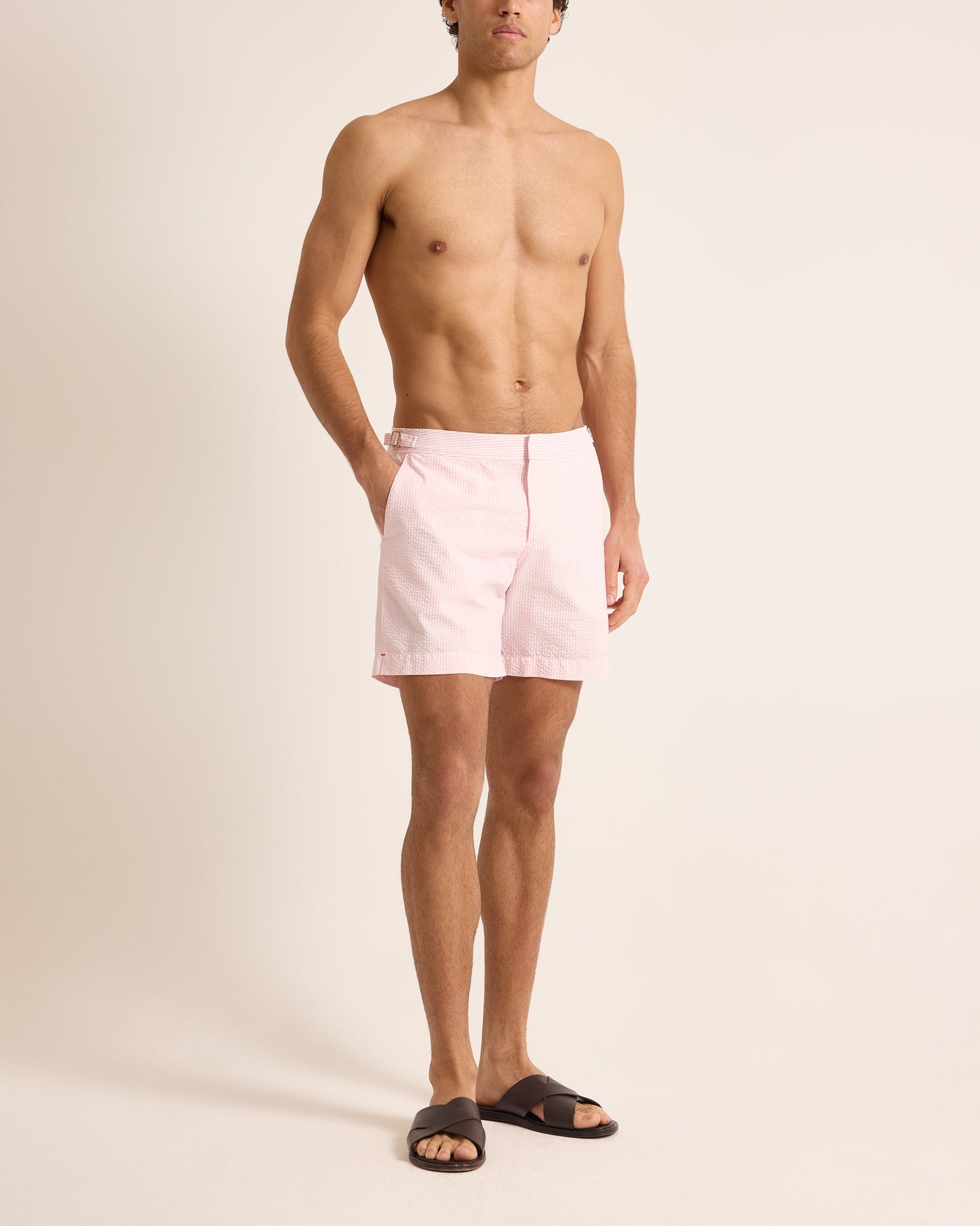 Man wearing light pink swim shorts on a beige background
