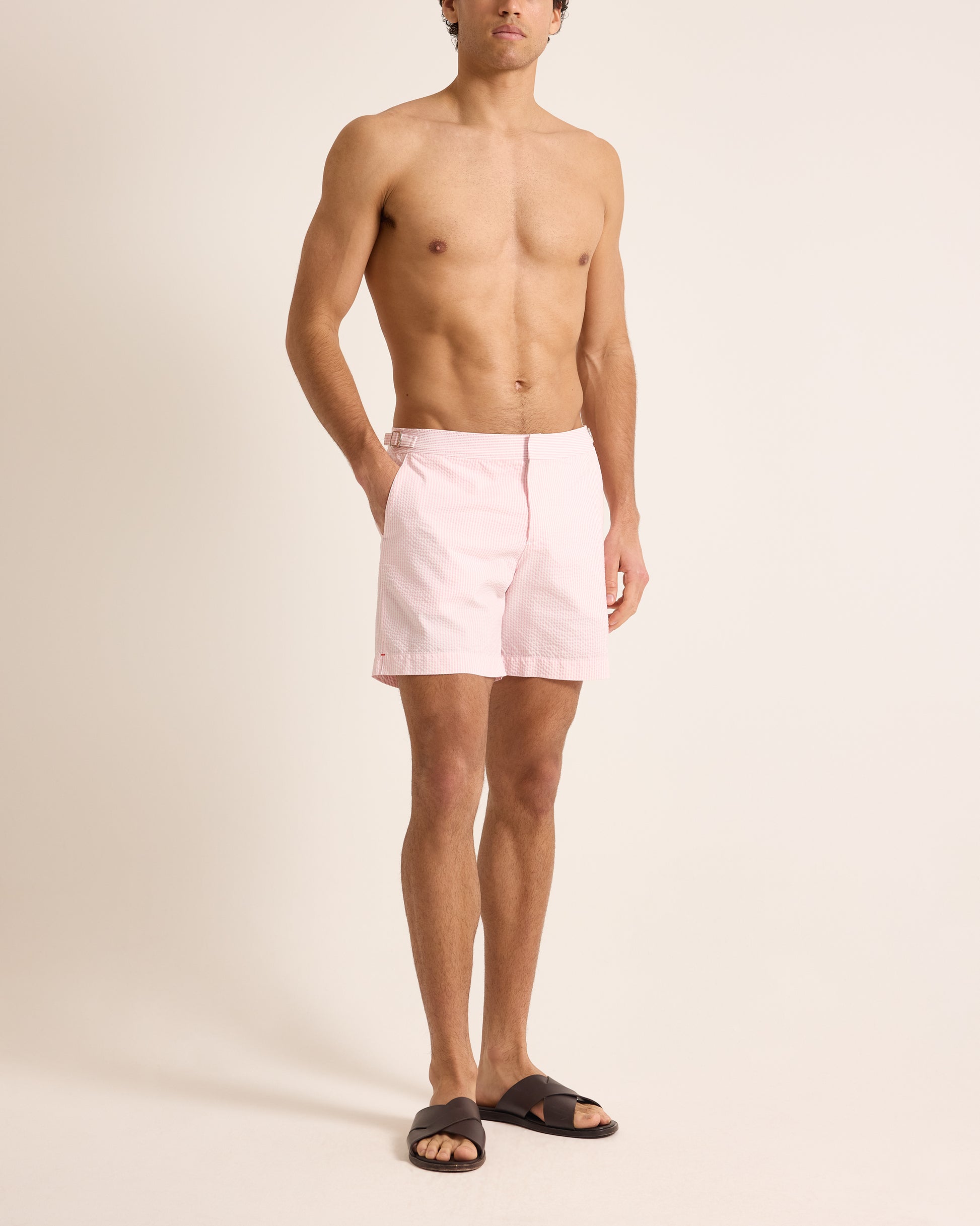 Man wearing light pink swim shorts on a beige background