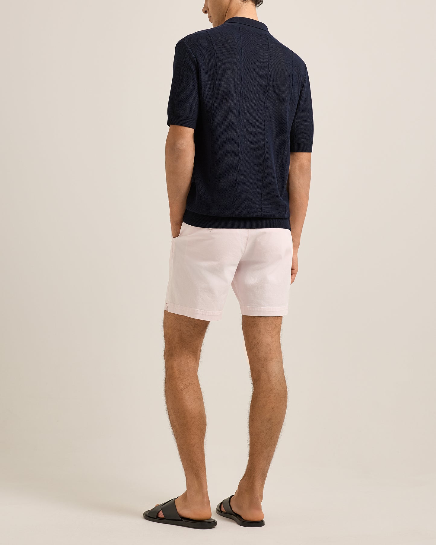 Man wearing a navy polo shirt and pink shorts on a beige background