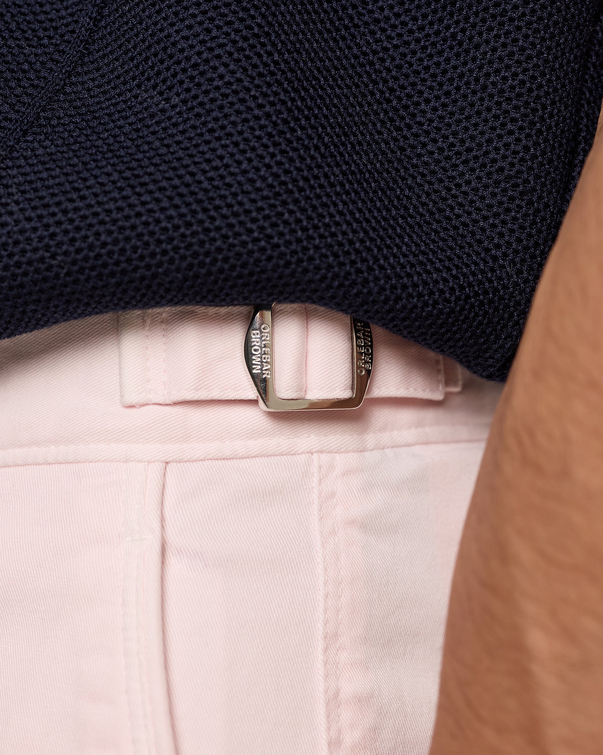 Close-up of a belt buckle on light pink pants with a dark textured shirt.