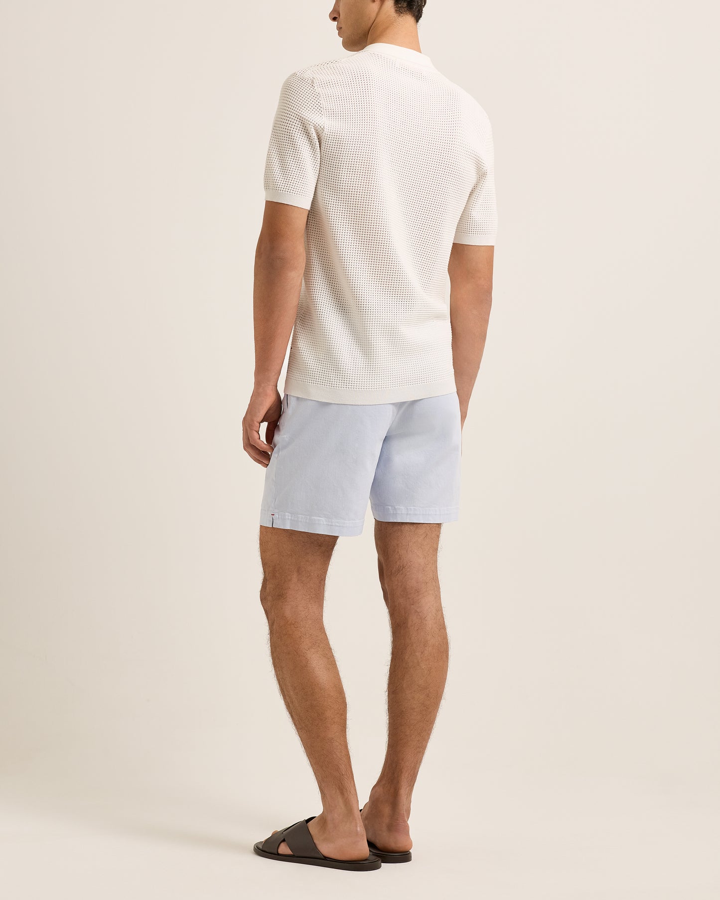 Man wearing a white t-shirt and light blue shorts on a beige background