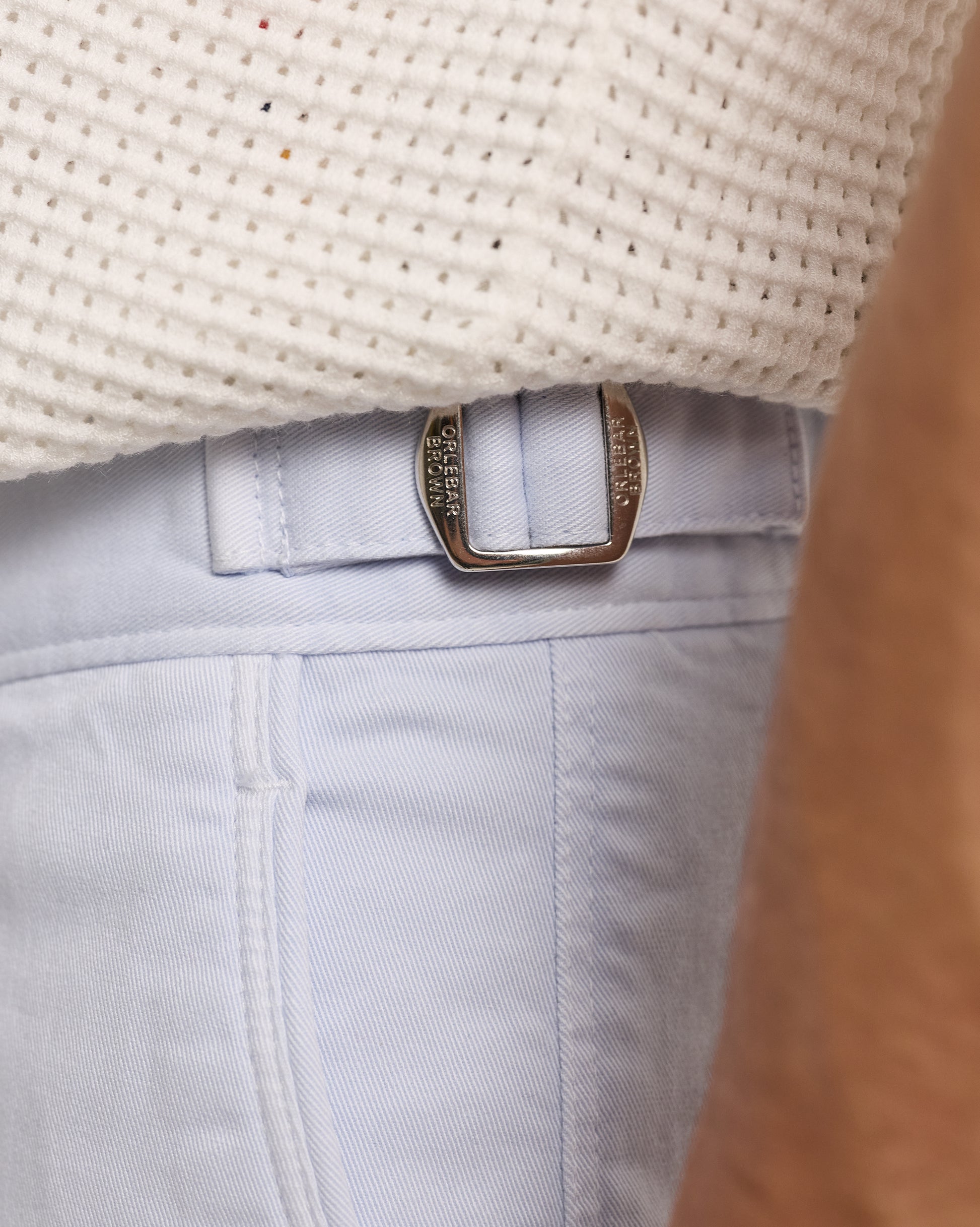 Close-up of light blue jeans with a belt and beige woven surface