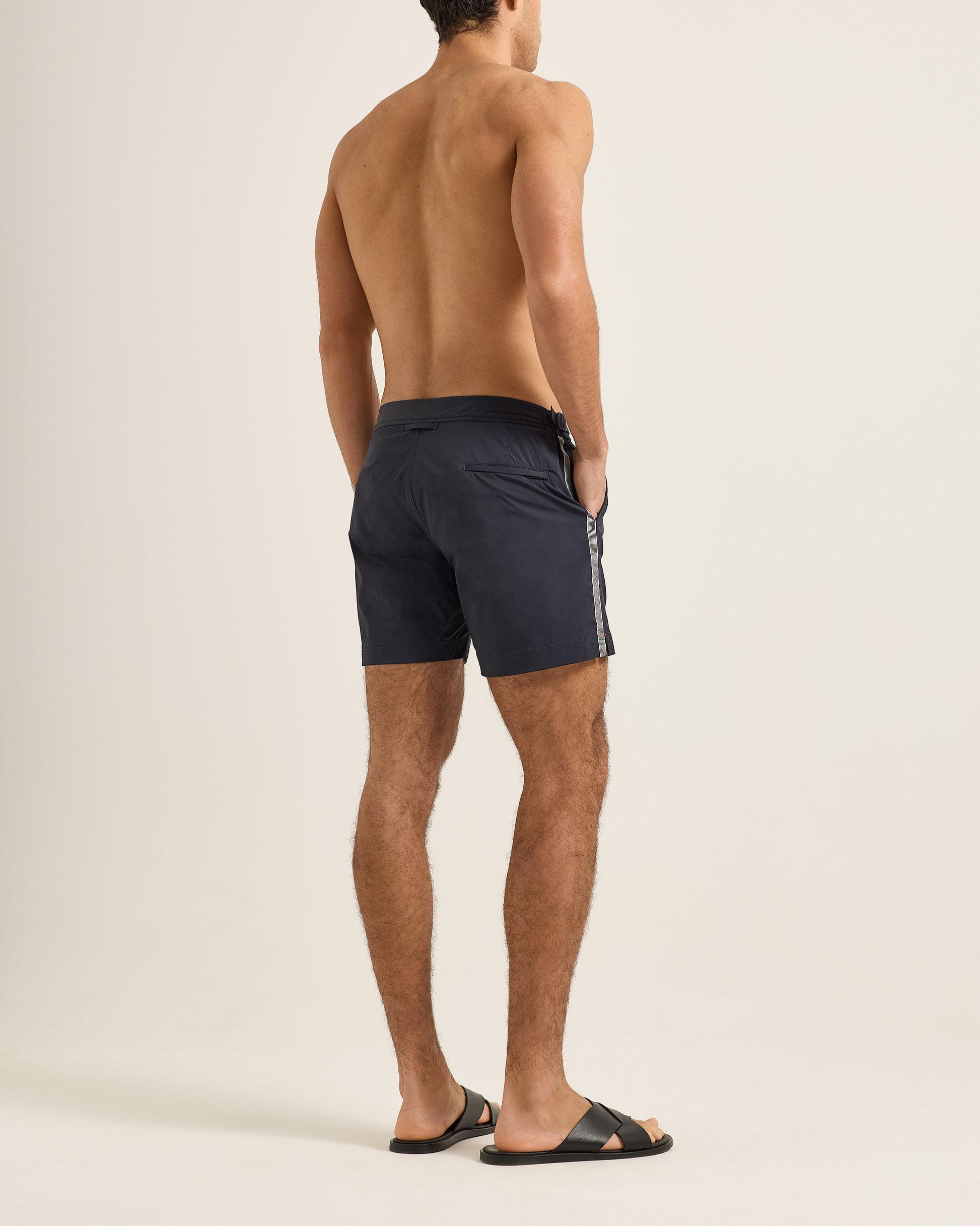 Man wearing navy swim shorts with white stripes on a beige background