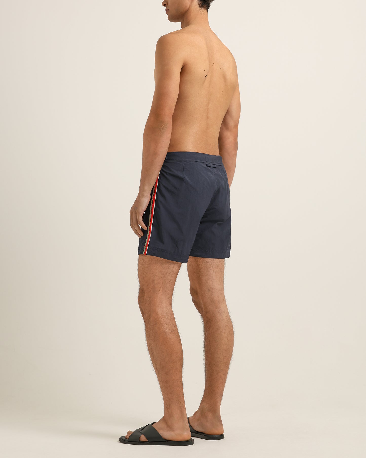 Man wearing navy swim shorts with red stripes on a beige background