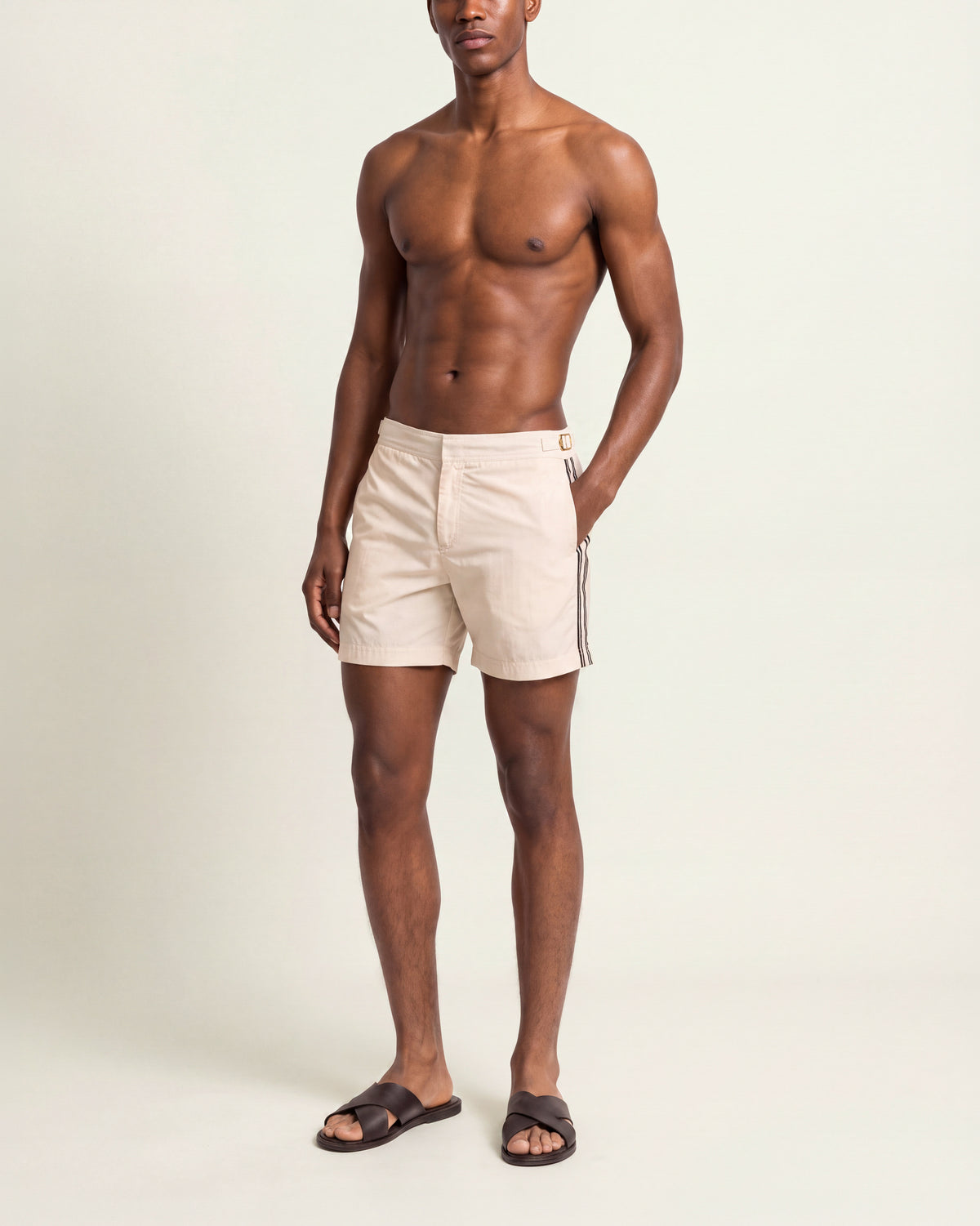 Man wearing a beige shorts with black stripes with brown sandals on a plain background