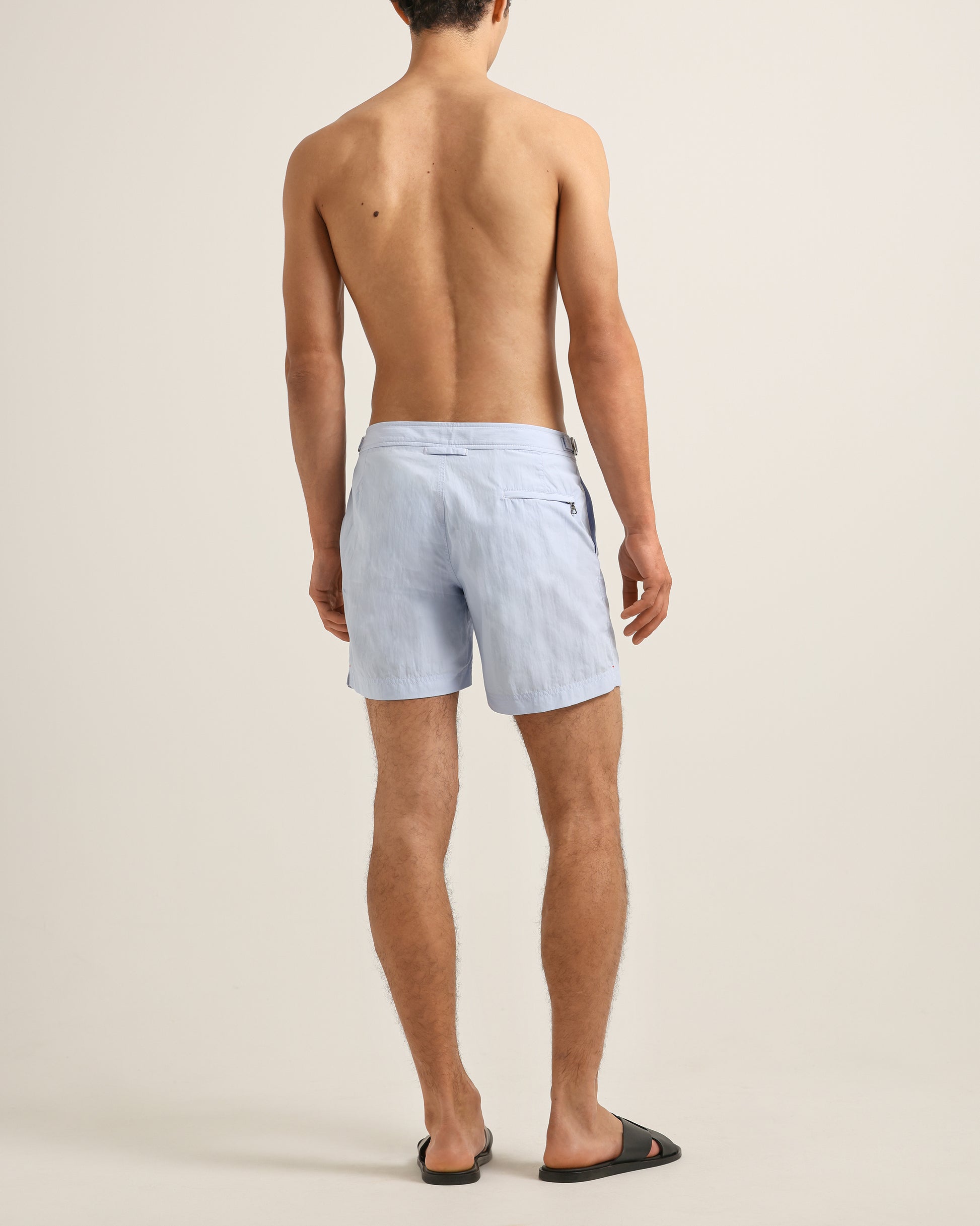 Man wearing light blue swim shorts on a beige background
