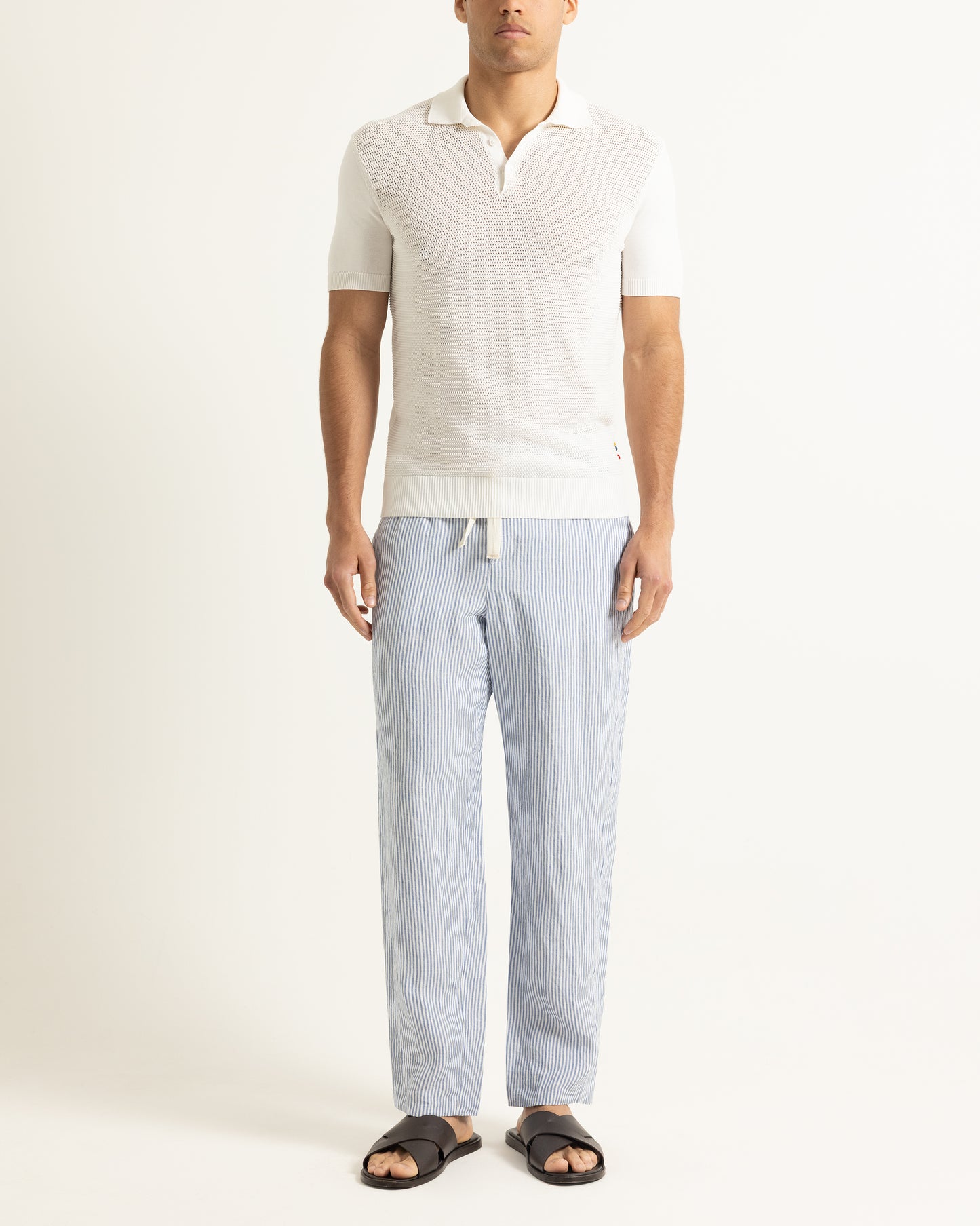 Man wearing a white polo shirt and light blue striped pants on a white background
