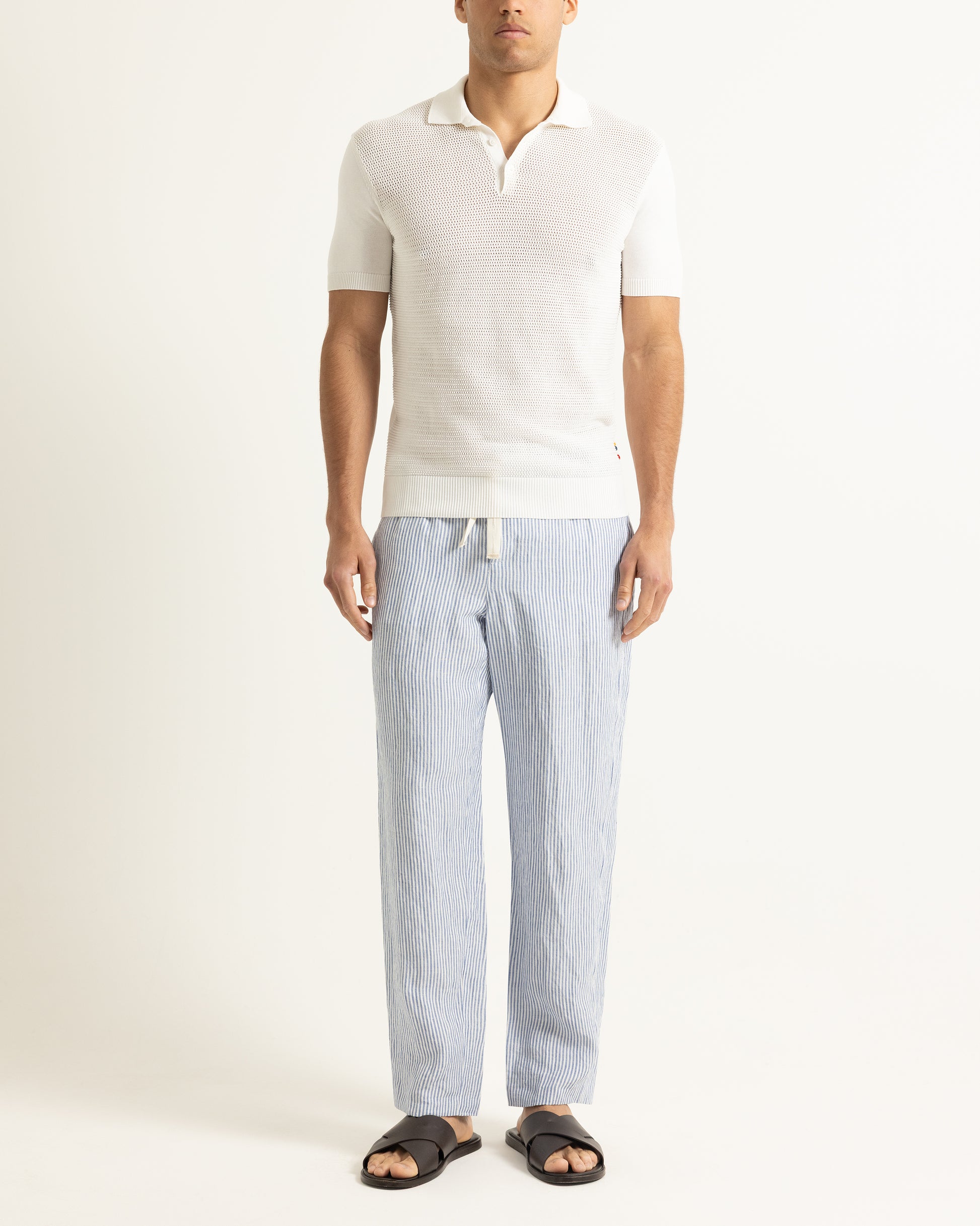 Man wearing a white polo shirt and light blue striped pants on a white background
