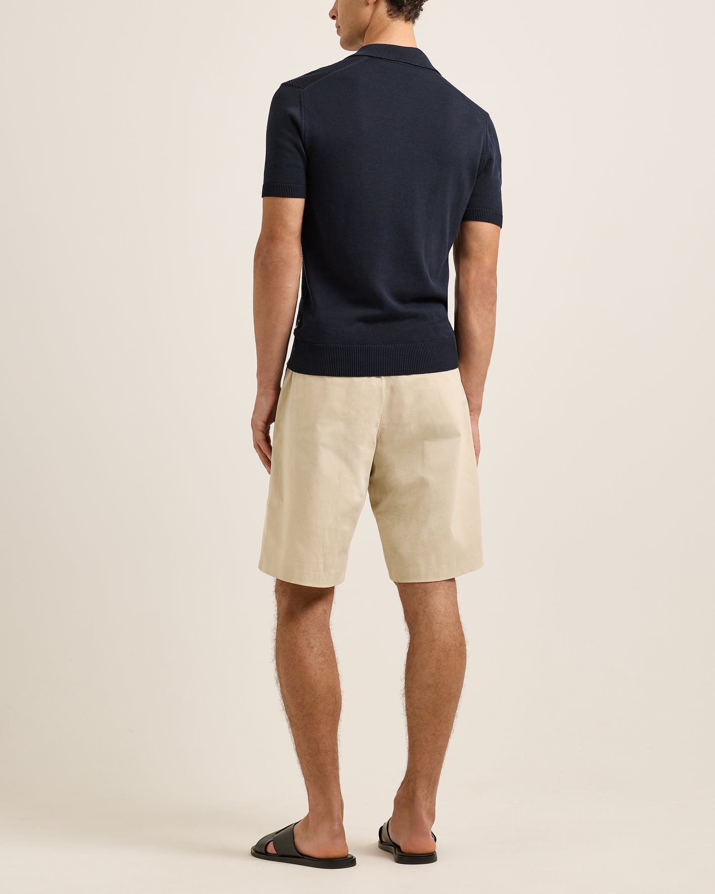 Man wearing a navy polo shirt and beige shorts on a plain background