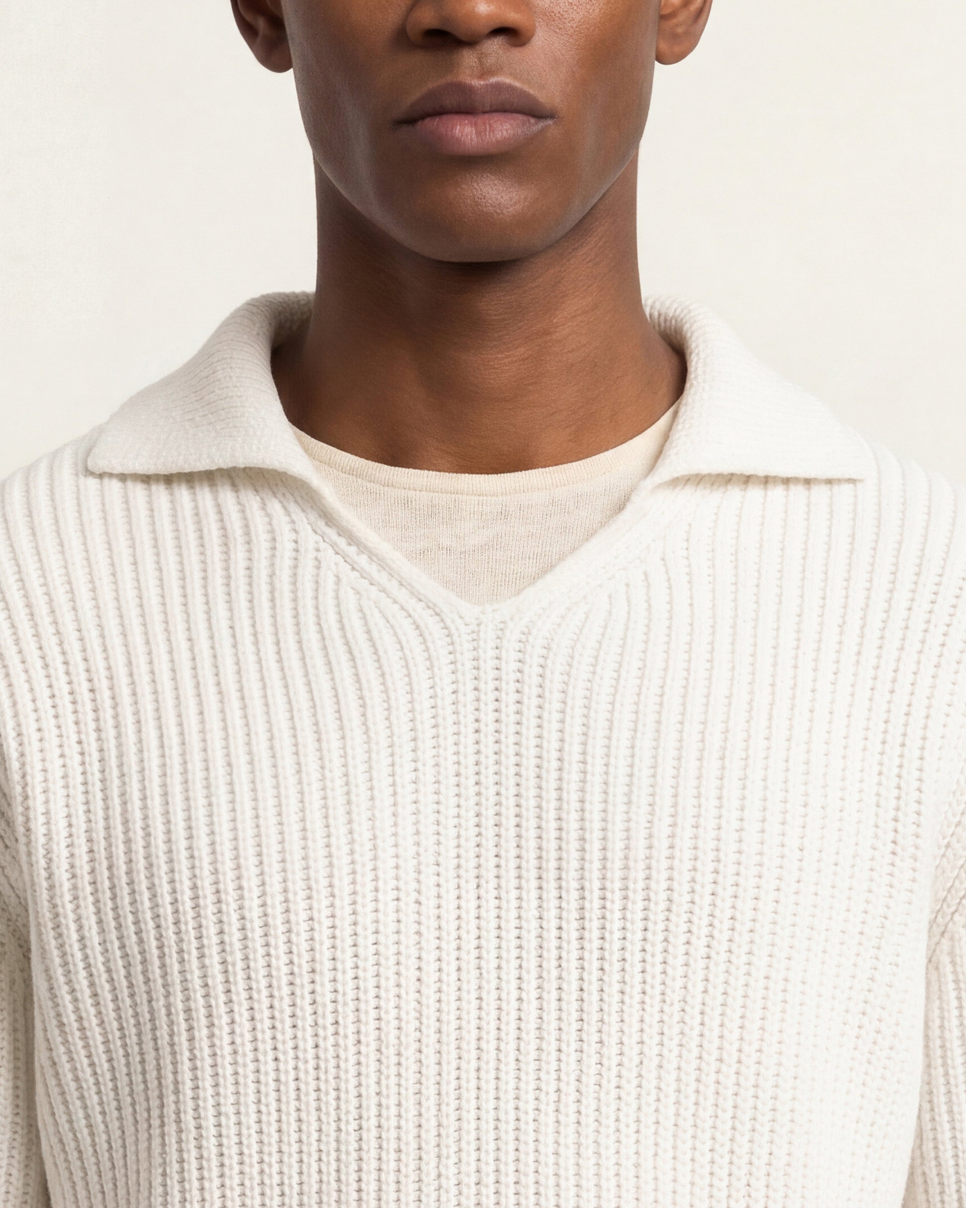Close-up of a model wearing a cream ribbed knit polo sweater over a matching cream crewneck shirt, against a plain light background.