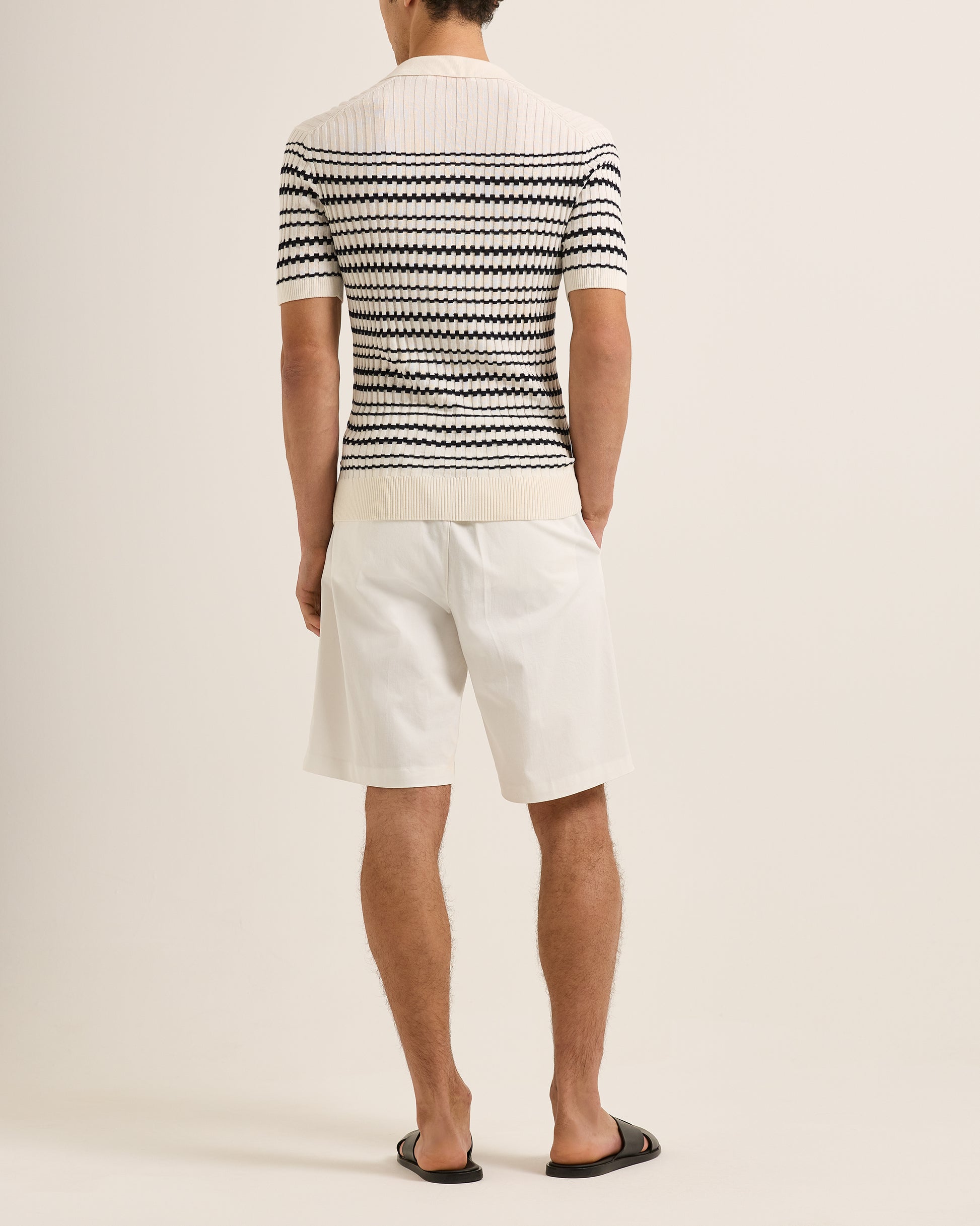 Person wearing a black and white striped polo and white shorts on a plain background