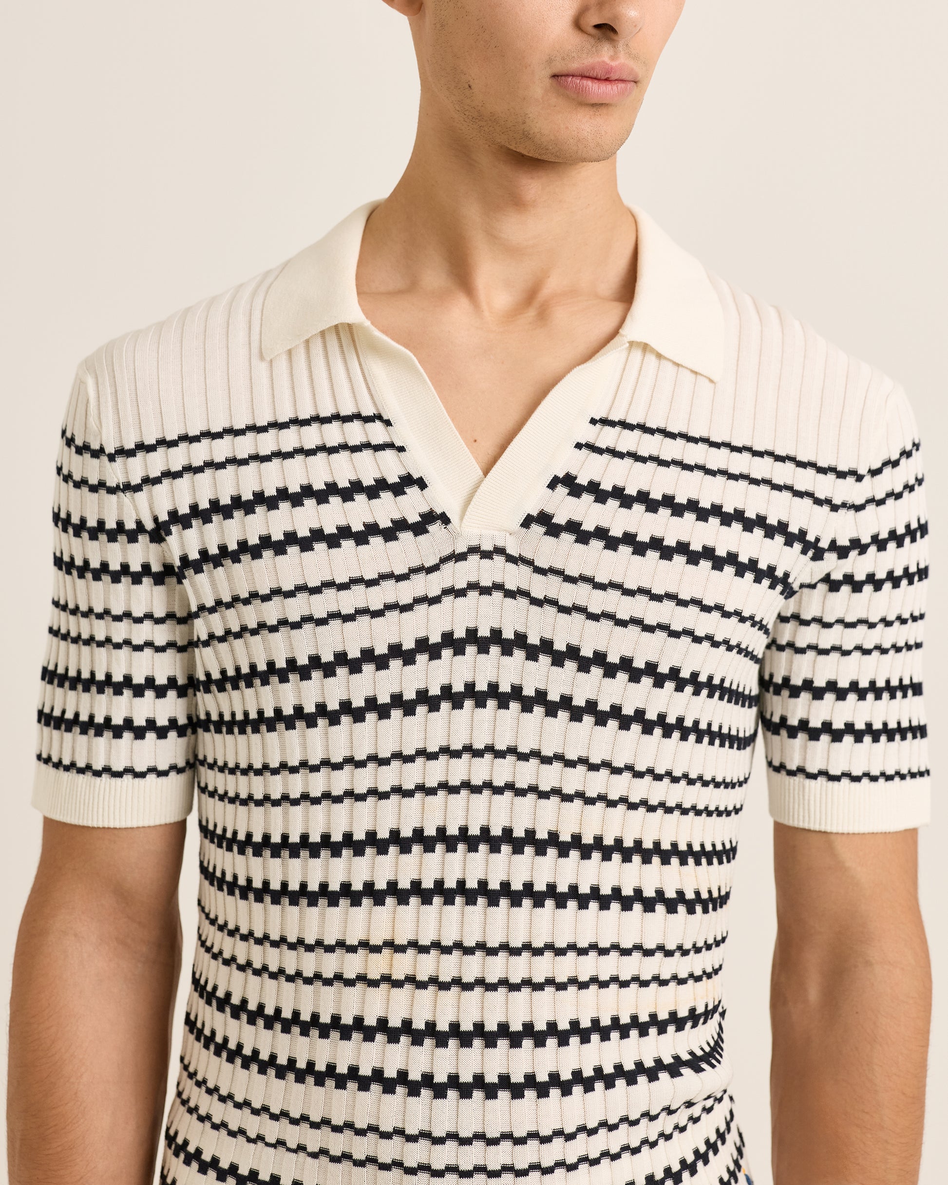 Man wearing a black and white striped polo over a collared shirt on a plain background