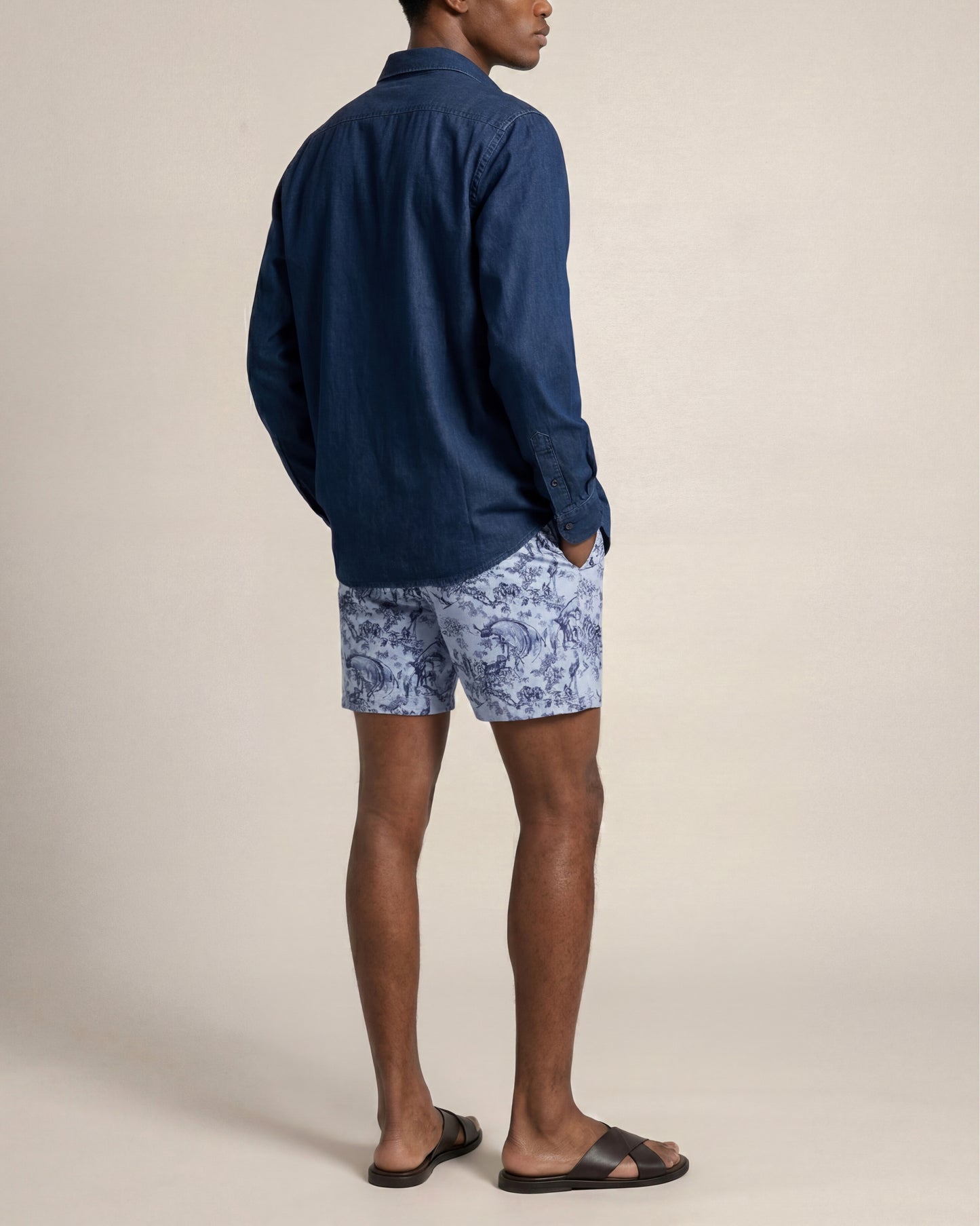 Man wearing a blue shirt and patterned shorts on a beige background